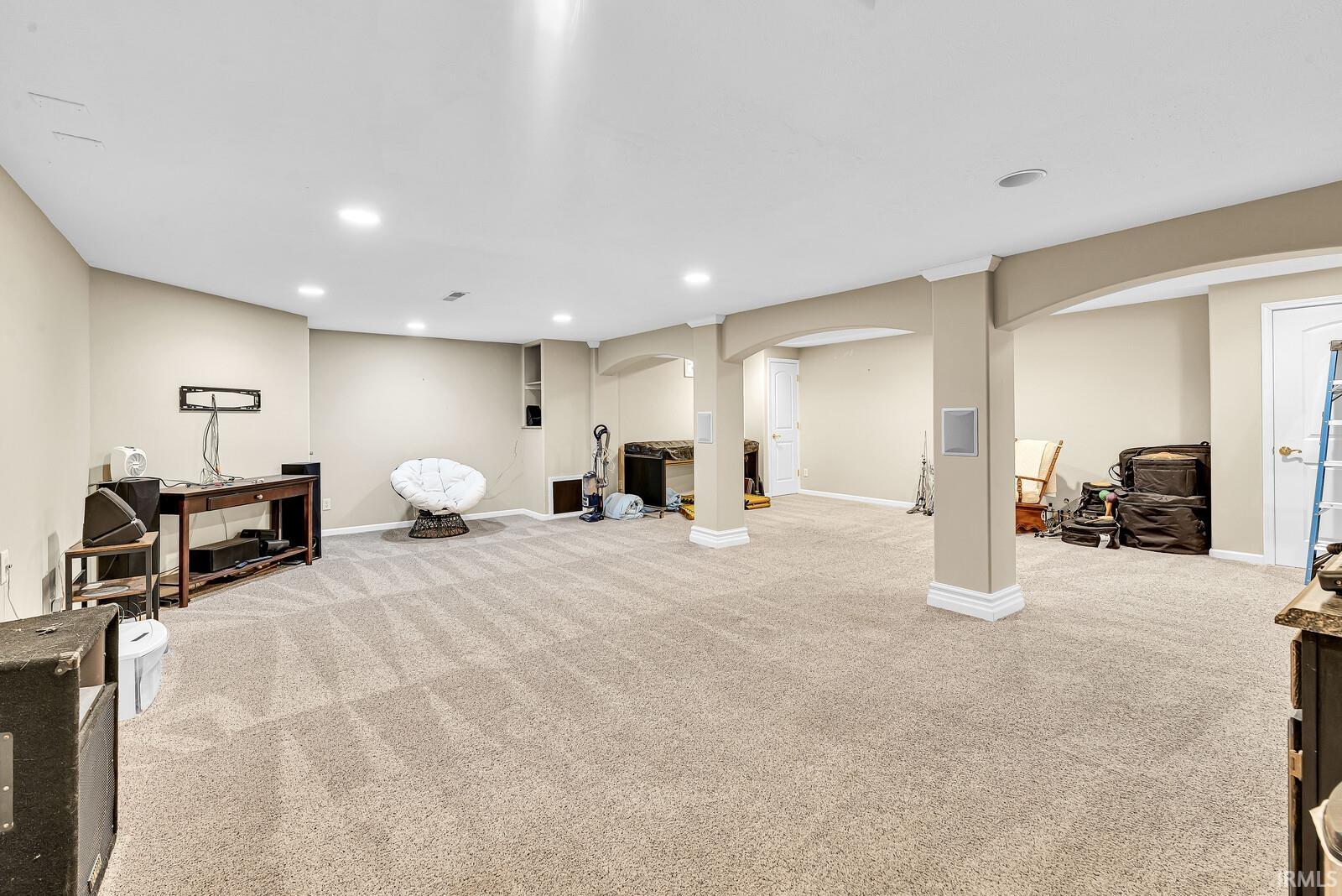 Spacious room featuring carpet flooring, recessed lighting, and architectural columns with arched openings