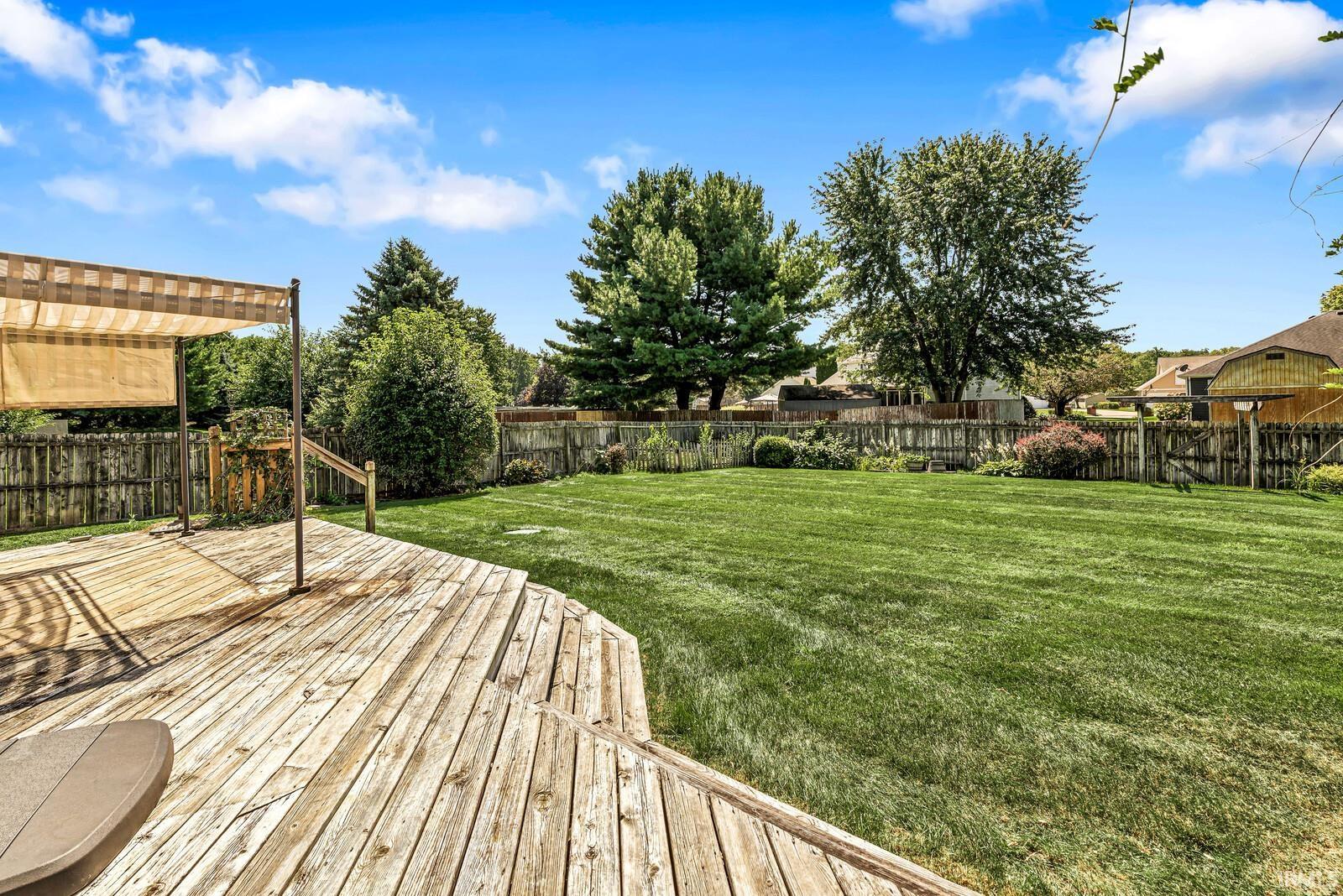 Expansive backyard featuring a manicured lawn, mature trees, and a wooden privacy fence