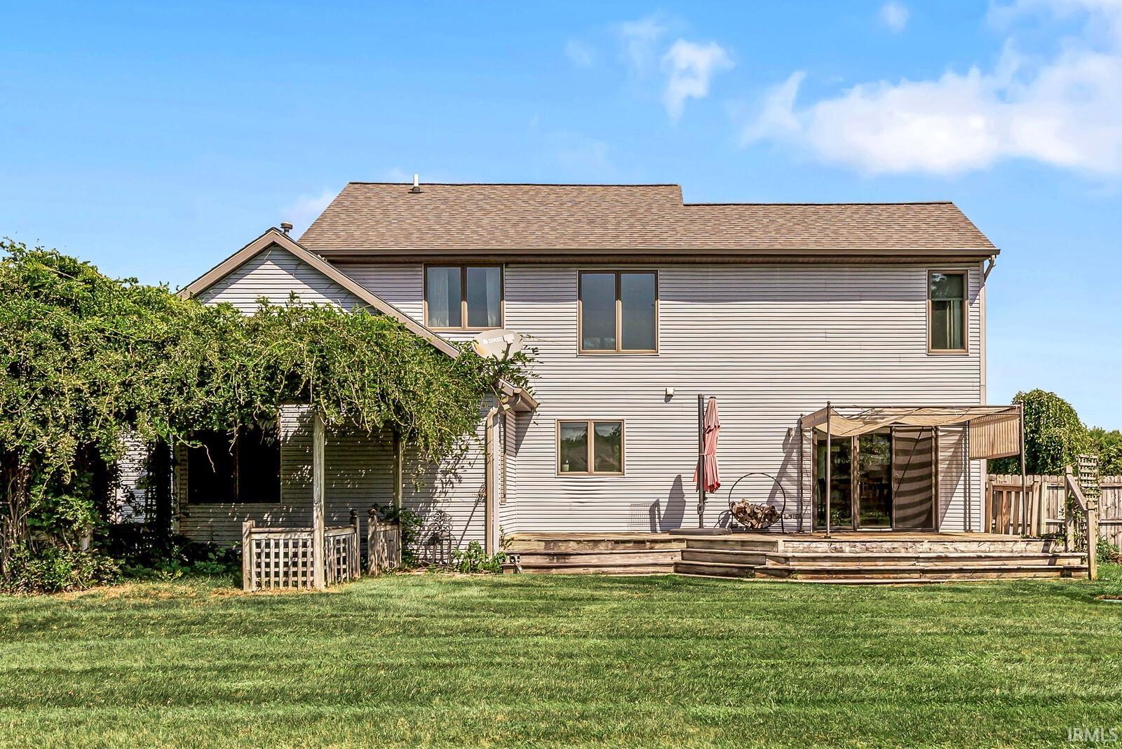Expansive green lawn with a multi-level wood deck featuring a covered area