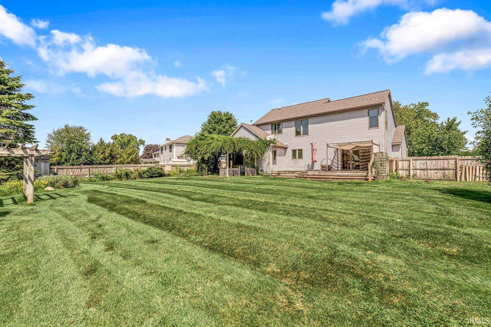 Expansive fenced yard with a wood deck, pergola-covered patio, and mature landscaping