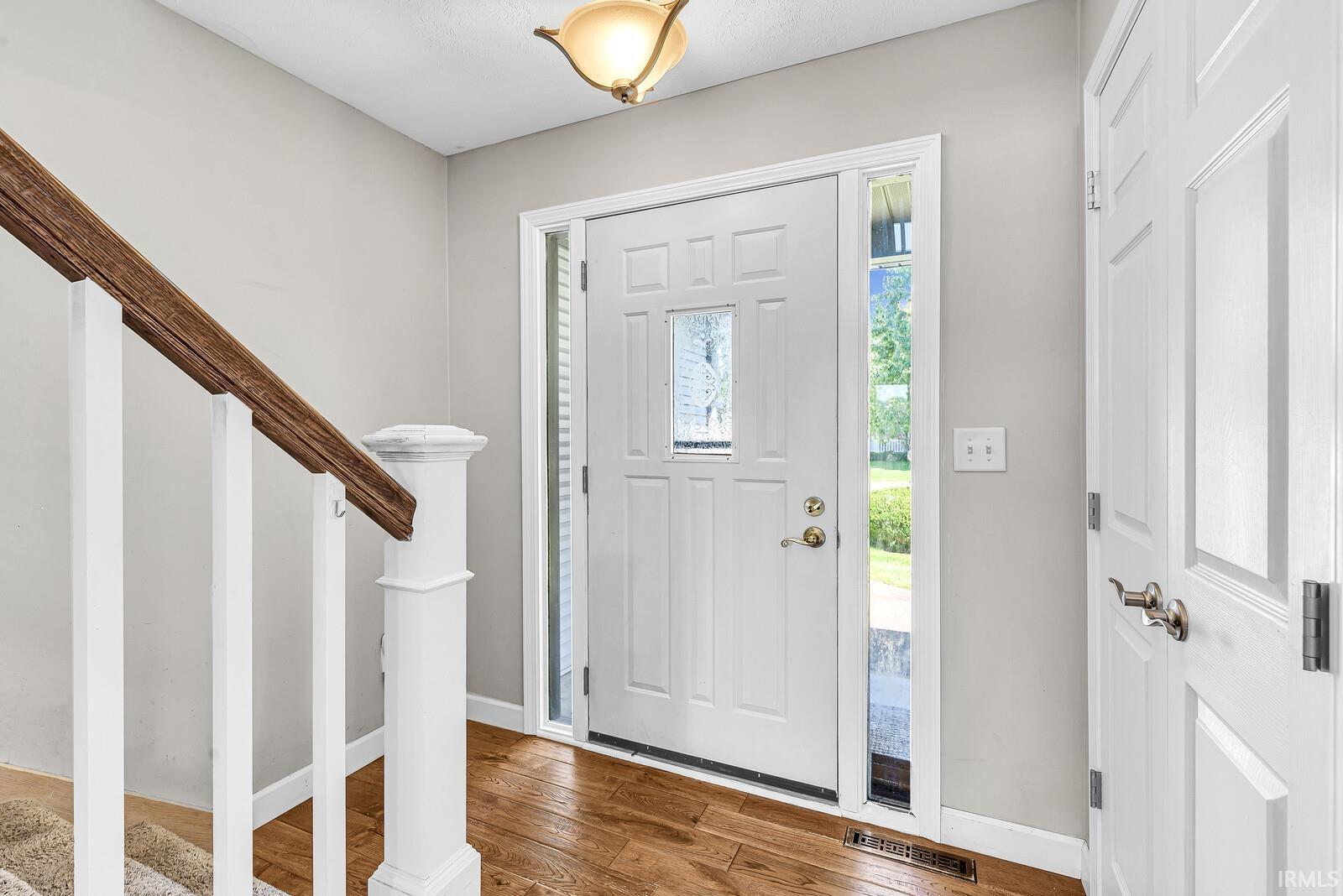 Hardwood flooring, painted interior door, sidelight windows, and a classic flush mount light fixture