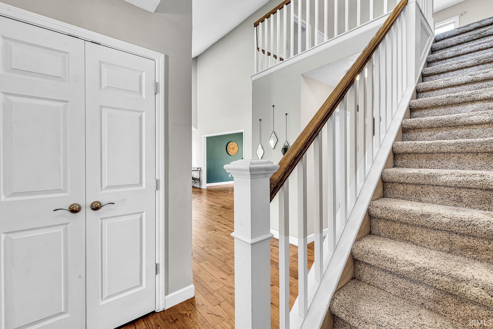 Two-story entry featuring wood-finish flooring, a carpeted staircase with white balusters, and a light wood-finish handrail