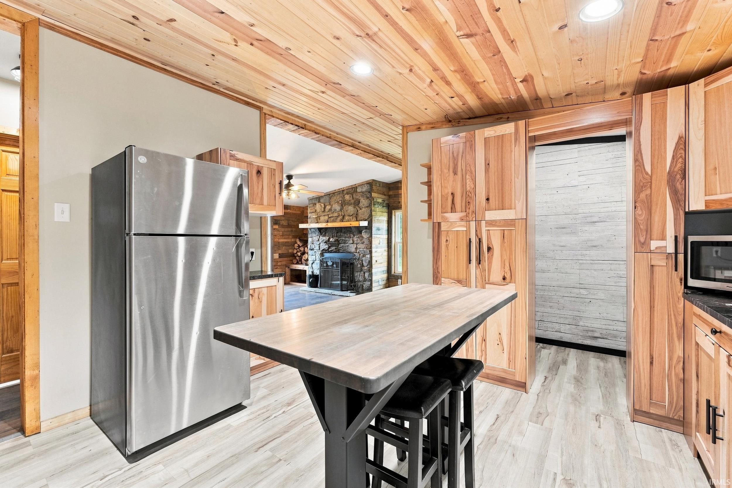 Wood-finish ceiling, stainless steel refrigerator, built-in wooden cabinetry, stone fireplace, and wood-finish flooring