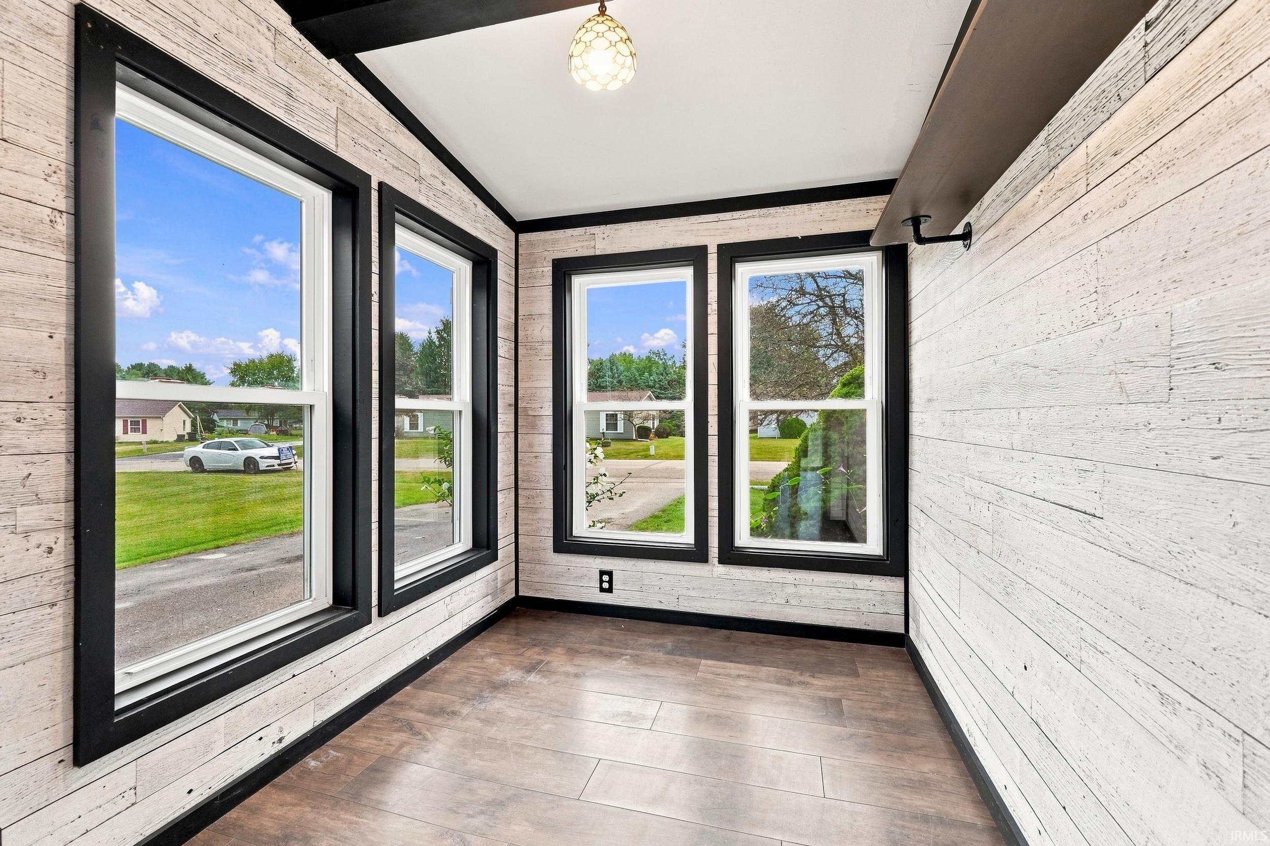 Room featuring multiple windows with black trim, wood-finish flooring, white shiplap walls, and a decorative ceiling light fixture