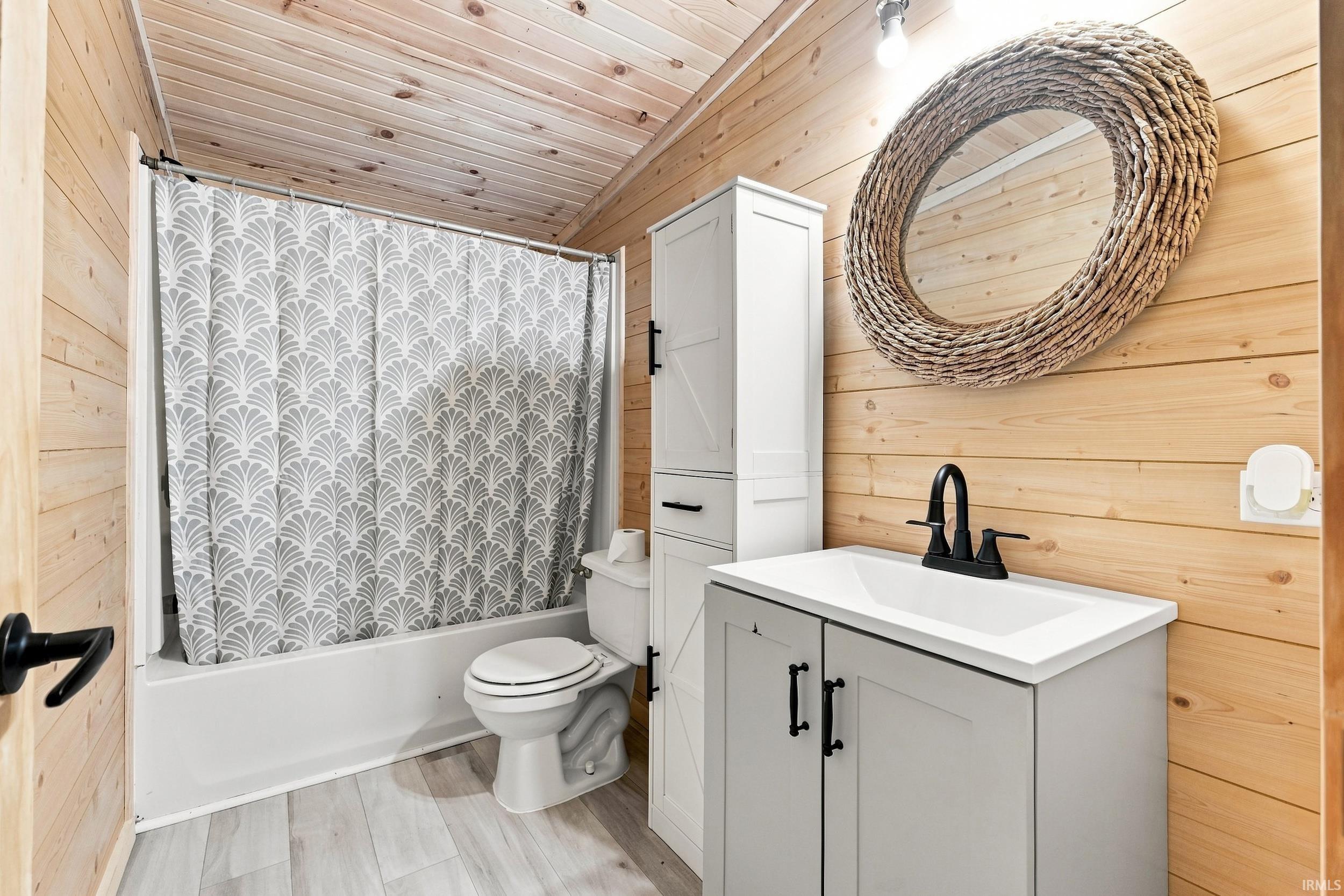 Wood-paneled walls and ceiling, white tub-shower combination, gray vanity with white countertop, black matte faucet, and wood-finish flooring