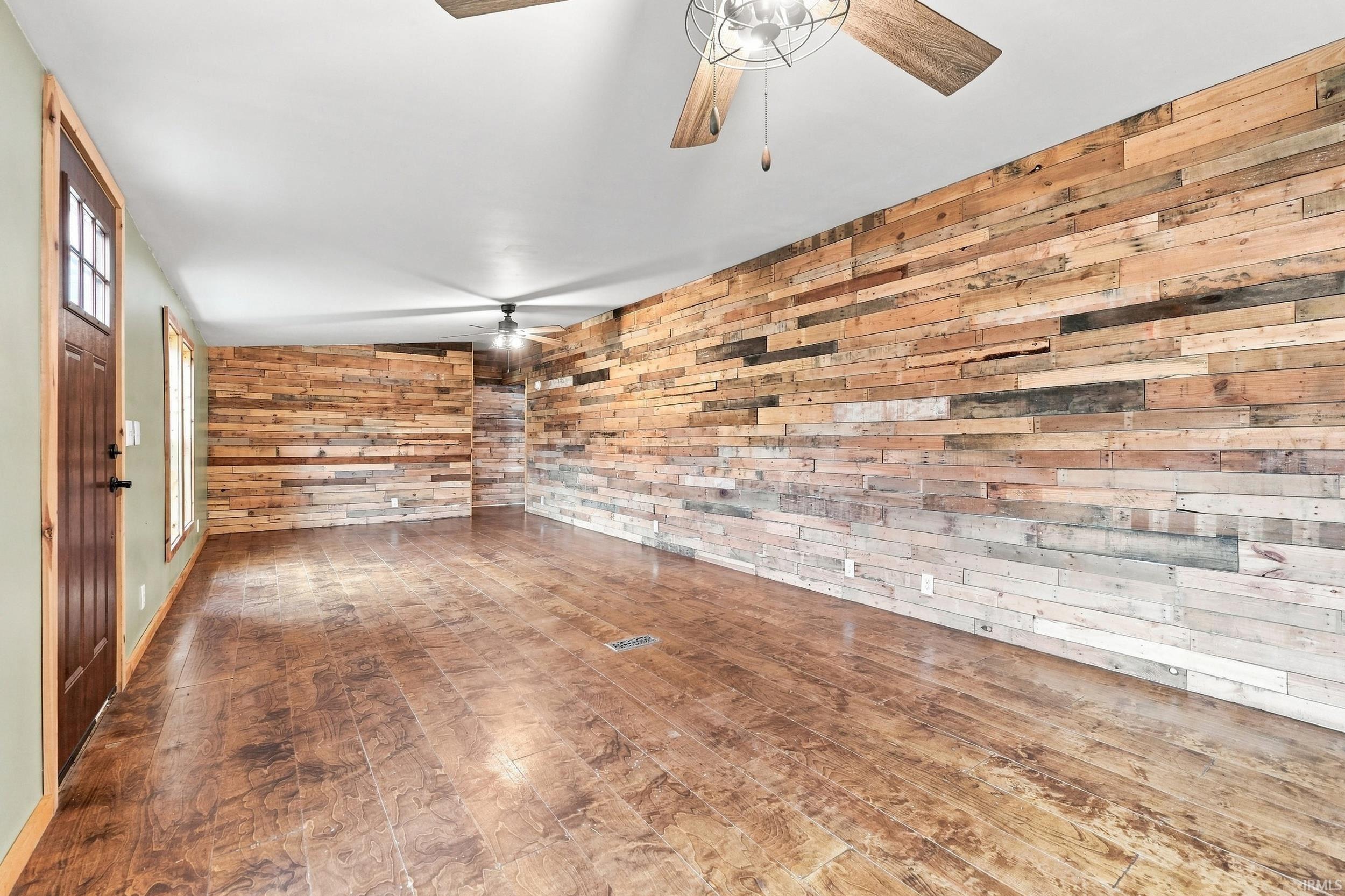 Wood-finish flooring, accent walls with horizontal wood paneling, wood-frame door with glass inserts, and ceiling fans with wood-finish blades
