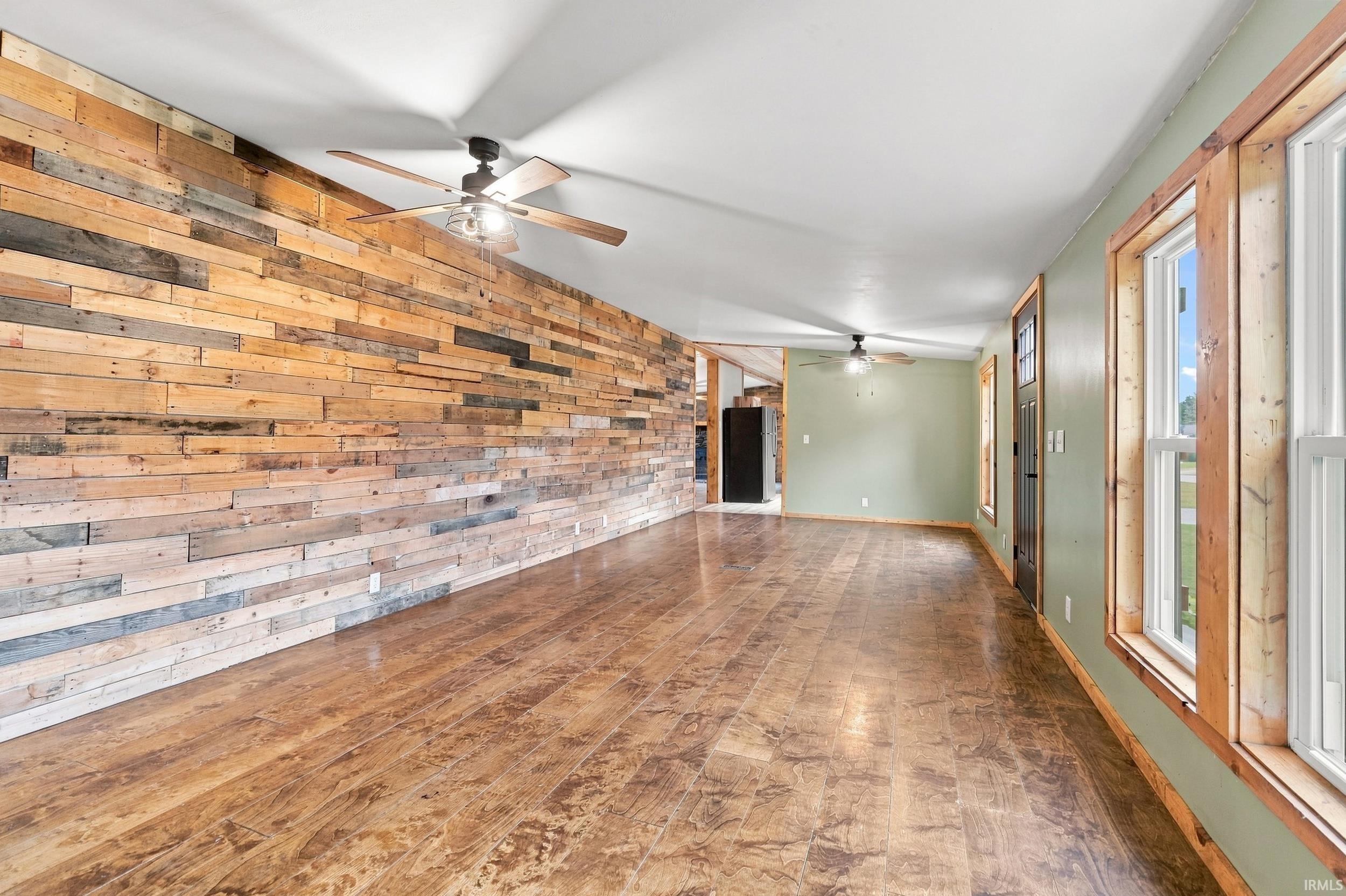 Expansive room featuring a wood-panel accent wall, wood-finish flooring, multiple windows, and ceiling fans