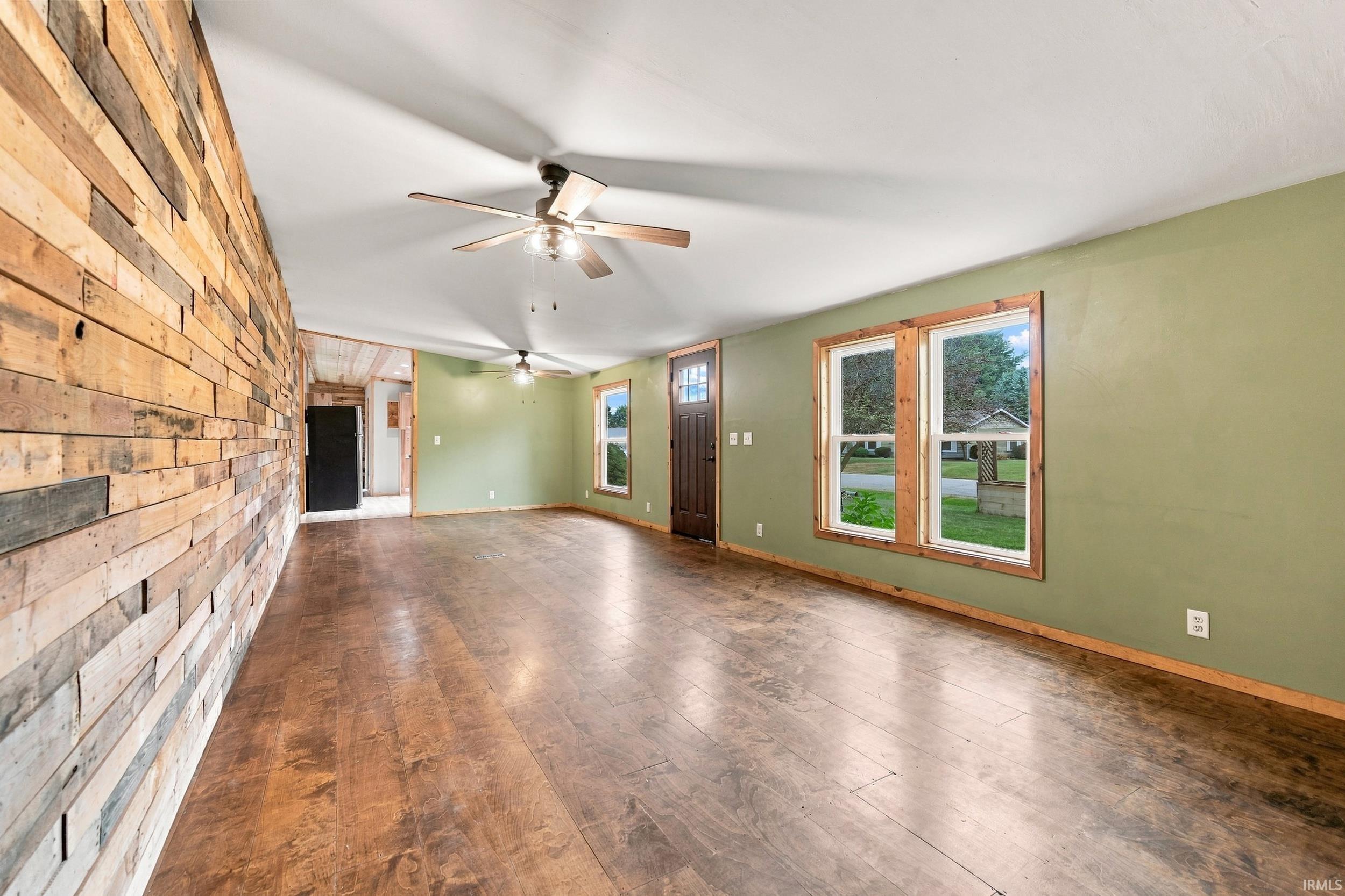 Wood-finish flooring, accent wall with horizontal wood planks, wood-framed windows, and a ceiling fan with integrated lighting