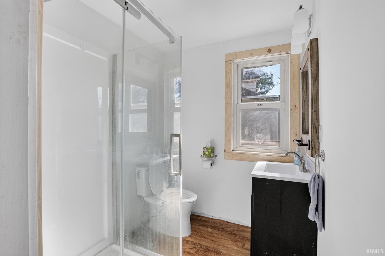 Glass-enclosed shower with swinging door, single vanity with integrated sink, vinyl floor and window with frosted glass