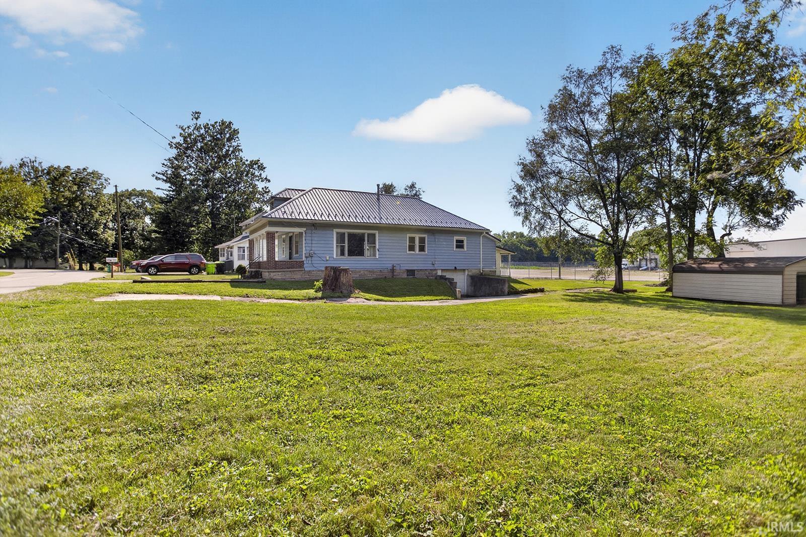 Expansive green lawn surrounds a light blue residence with a metal roof, and gravel path leading to basement garage