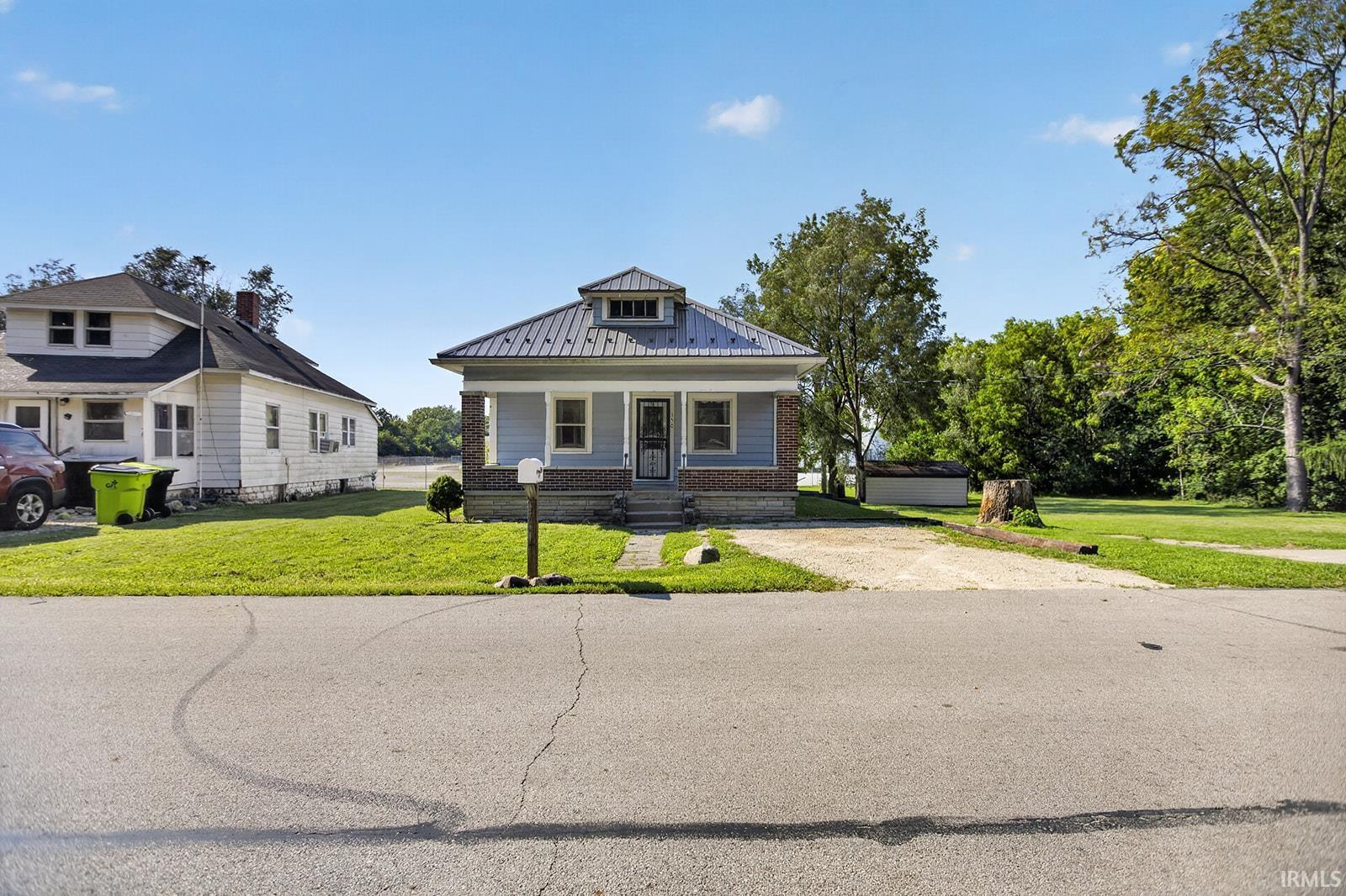 Bungalow style home featuring a gray metal roof, light blue siding, a covered front porch, a gravel driveway
