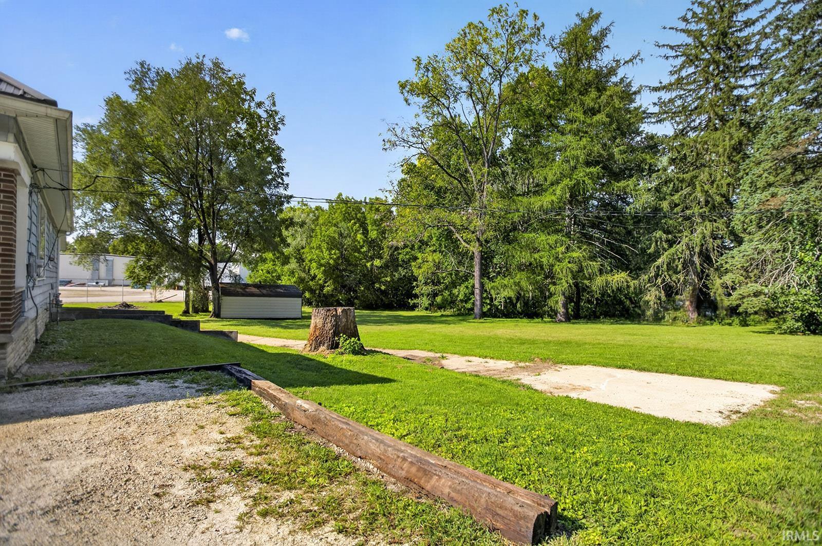 Expansive lawn area with a detached storage shed, mature trees, and a gravel pathway leading to basement garage