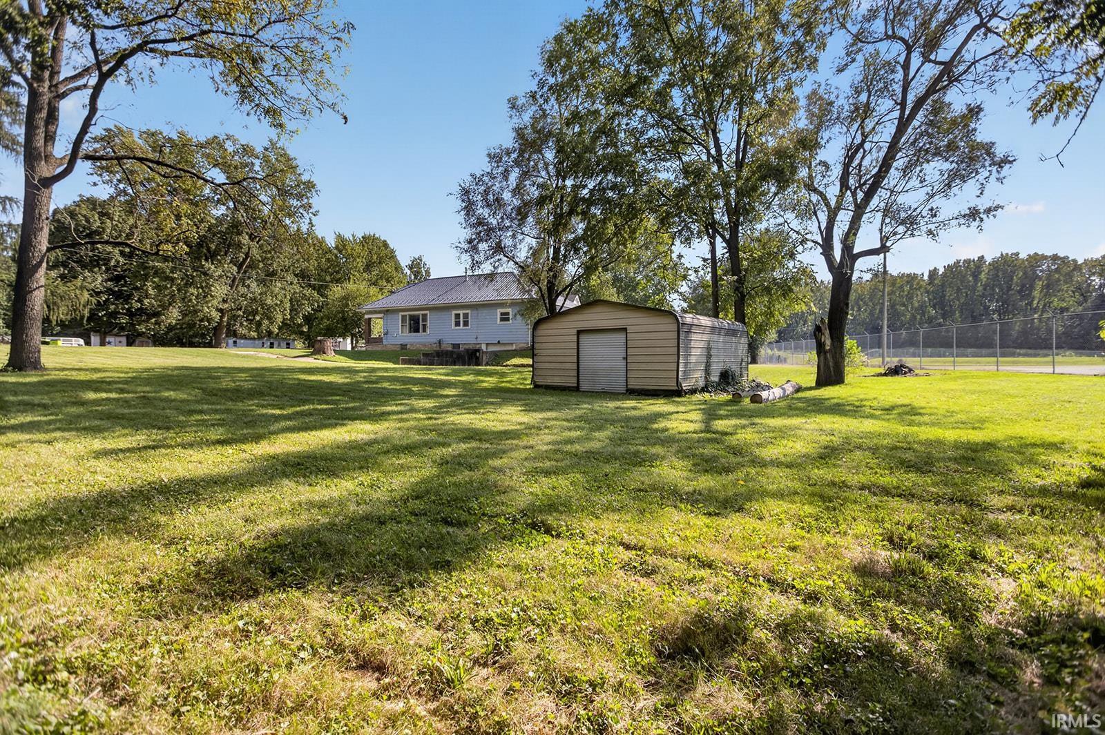 Expansive yard space featuring a metal storage shed, mature trees, and a distant property with light blue siding and a dark roof