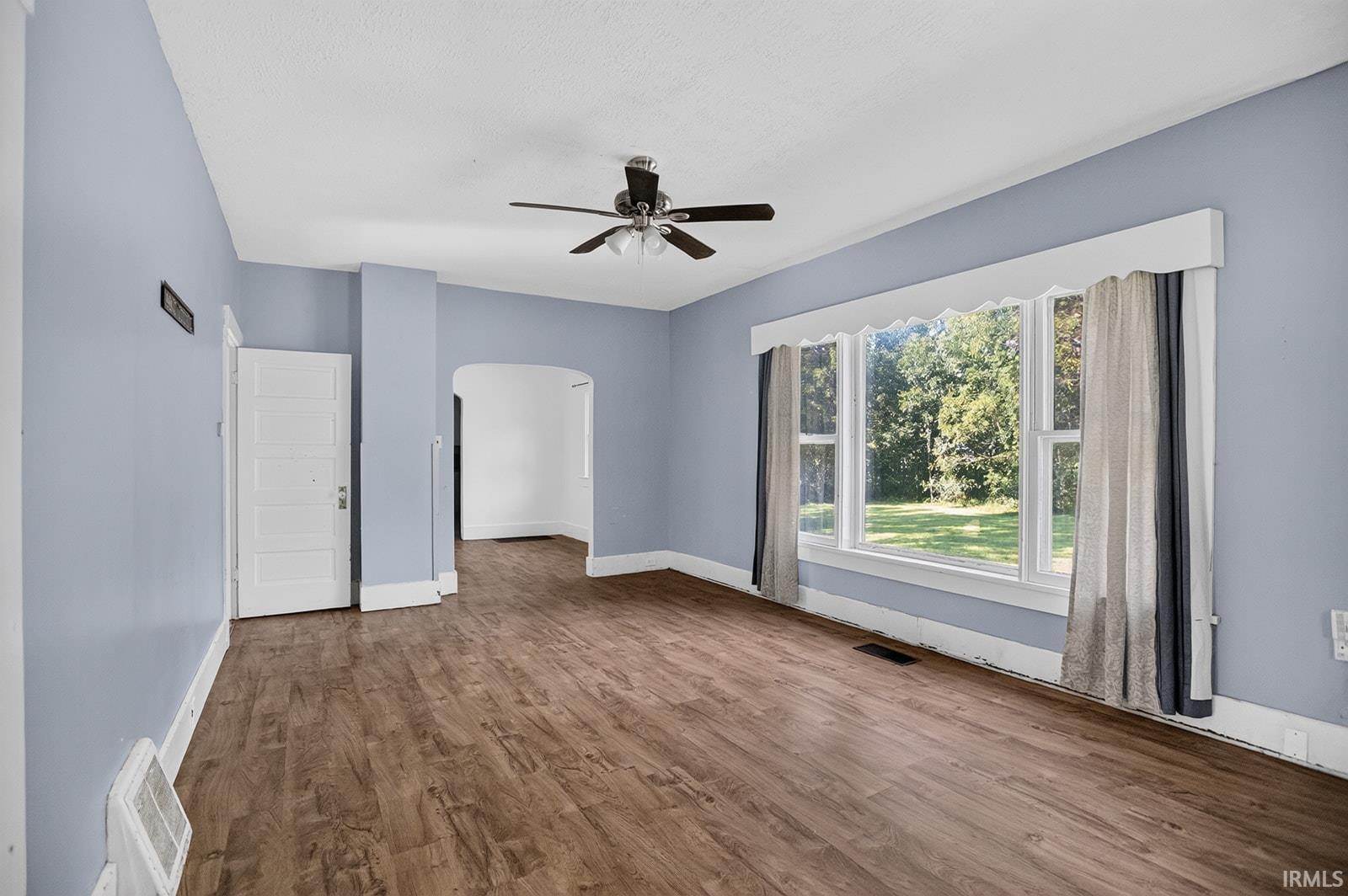 vinyl flooring, ceiling fan, wide window, arched doorway, and white trim