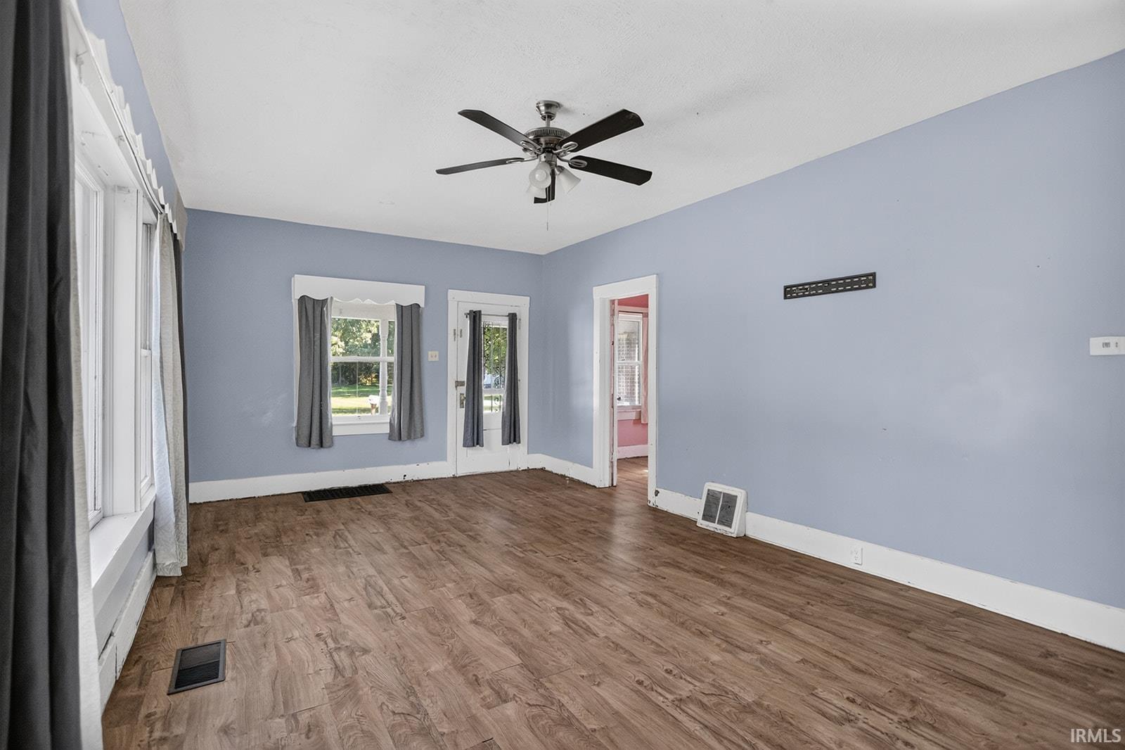Wood-finish flooring, ceiling fan, and multiple windows with white trim