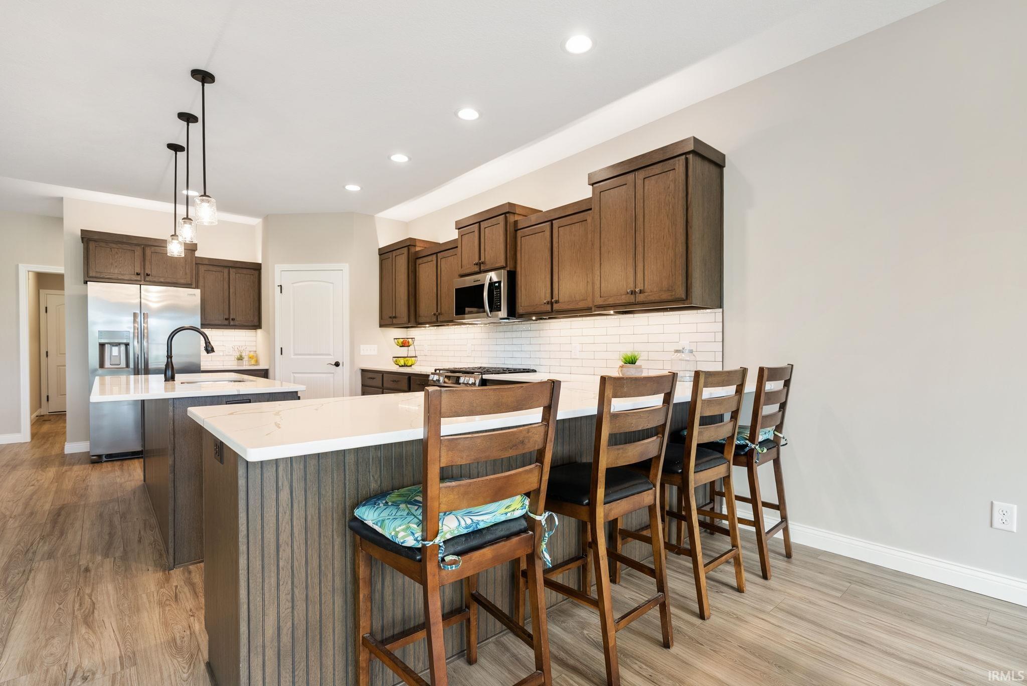 Kitchen featuring wood-finish flooring, two kitchen islands with solid surface countertops, dark wood cabinetry, a subway tile backsplash, and stainless steel appliances