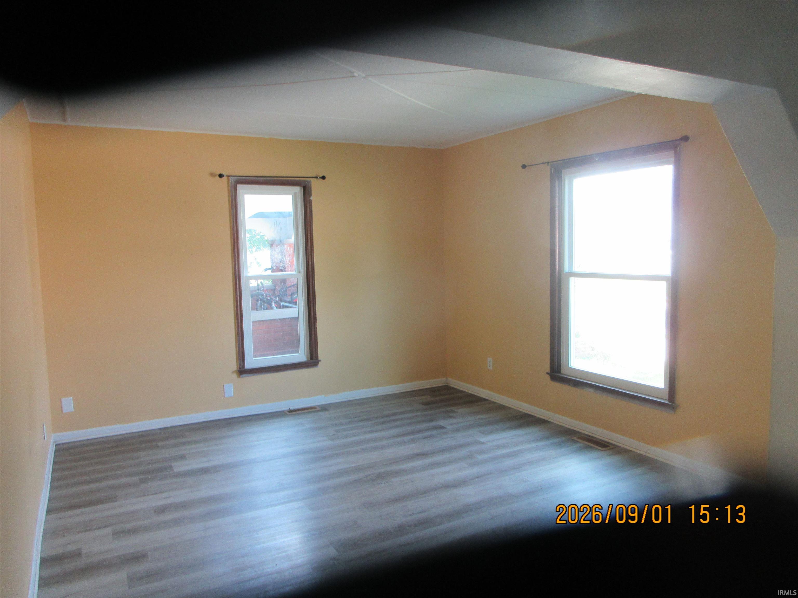 Neutral-toned walls, wood-finish flooring, and two windows with dark trim