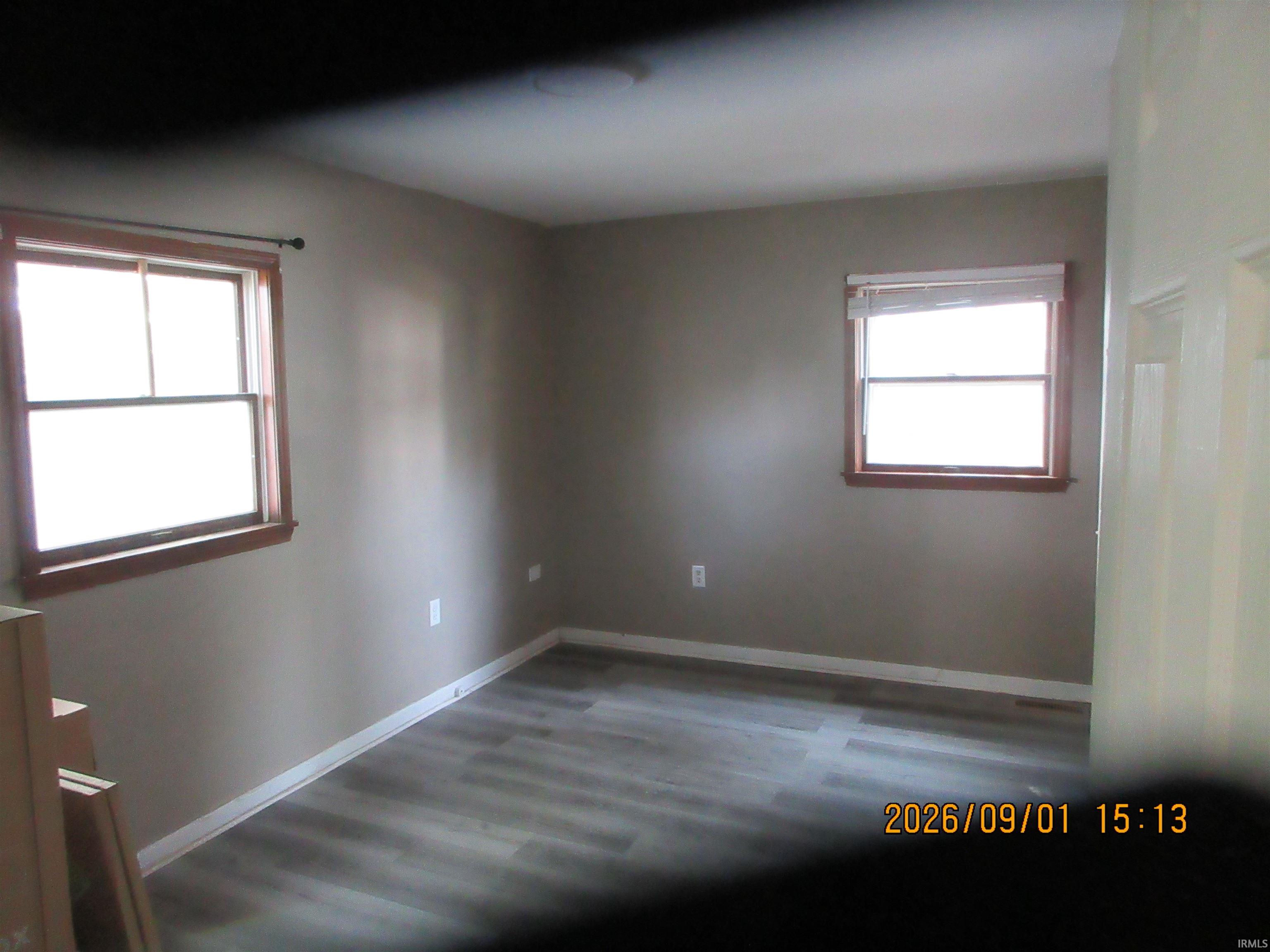 Wood-finish flooring with white baseboards, tan walls, and two windows with wood trim