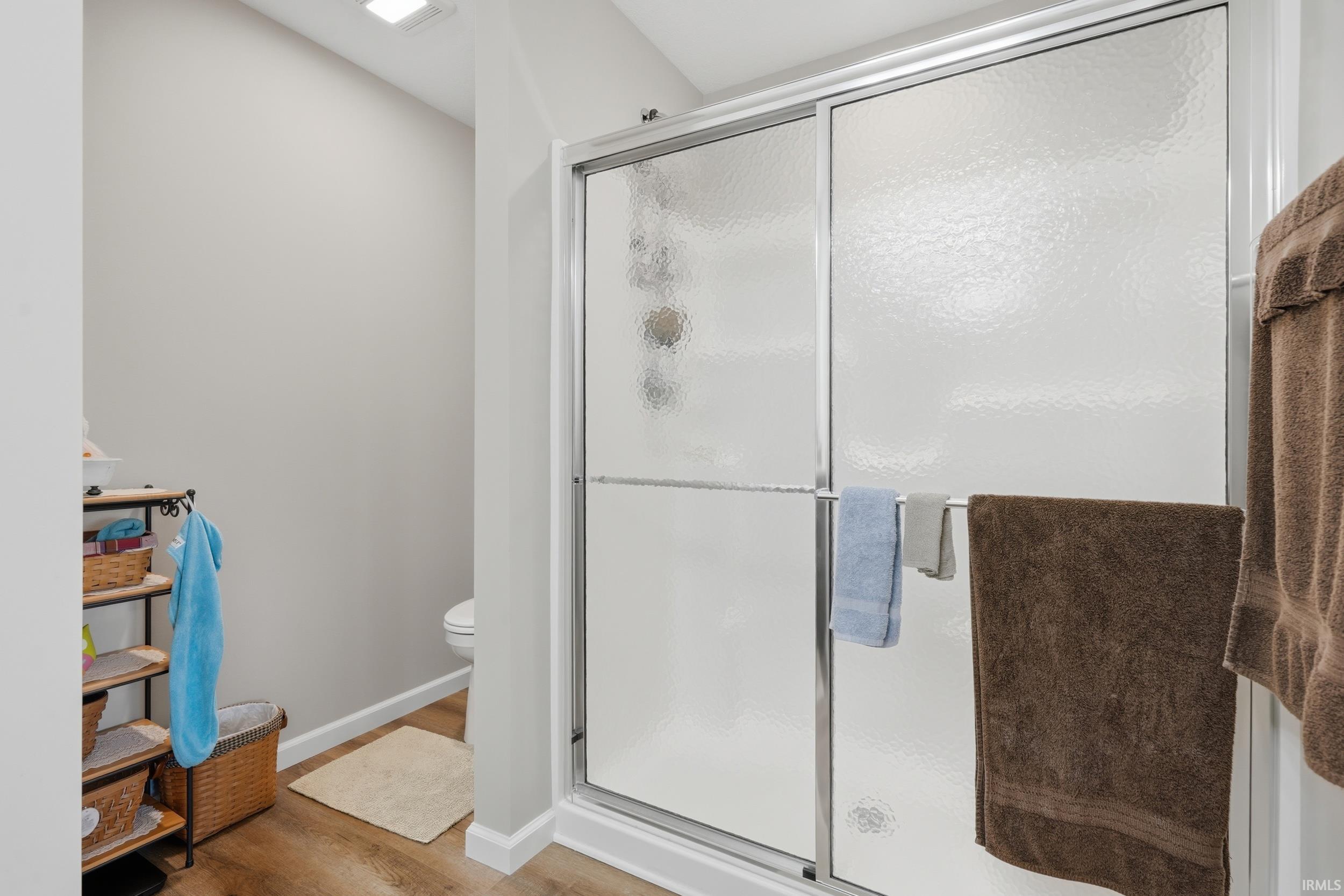 Shower enclosure with sliding frosted glass doors, chrome hardware, and wood-finish flooring