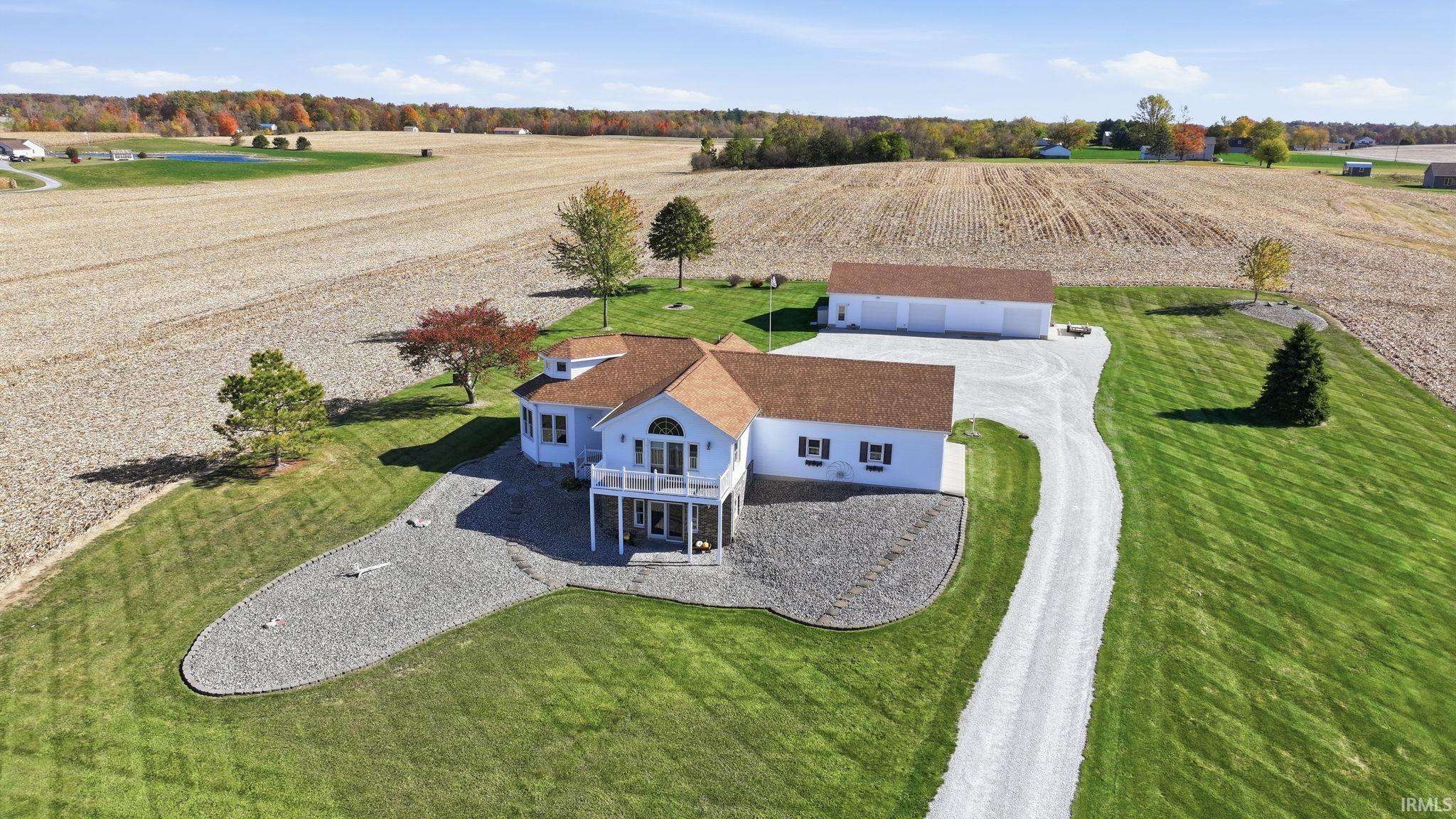 Multi-level residence featuring a shingled roof, elevated second-story deck, stone-finish exterior accents, attached garage, and gravel driveway situated on a expansive parcel