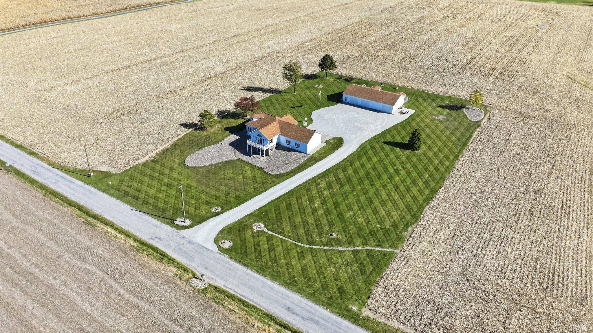 Aerial perspective of a detached residence and secondary structure, featuring expansive lawn space, gravel driveway, and a multi-level exterior roofline
