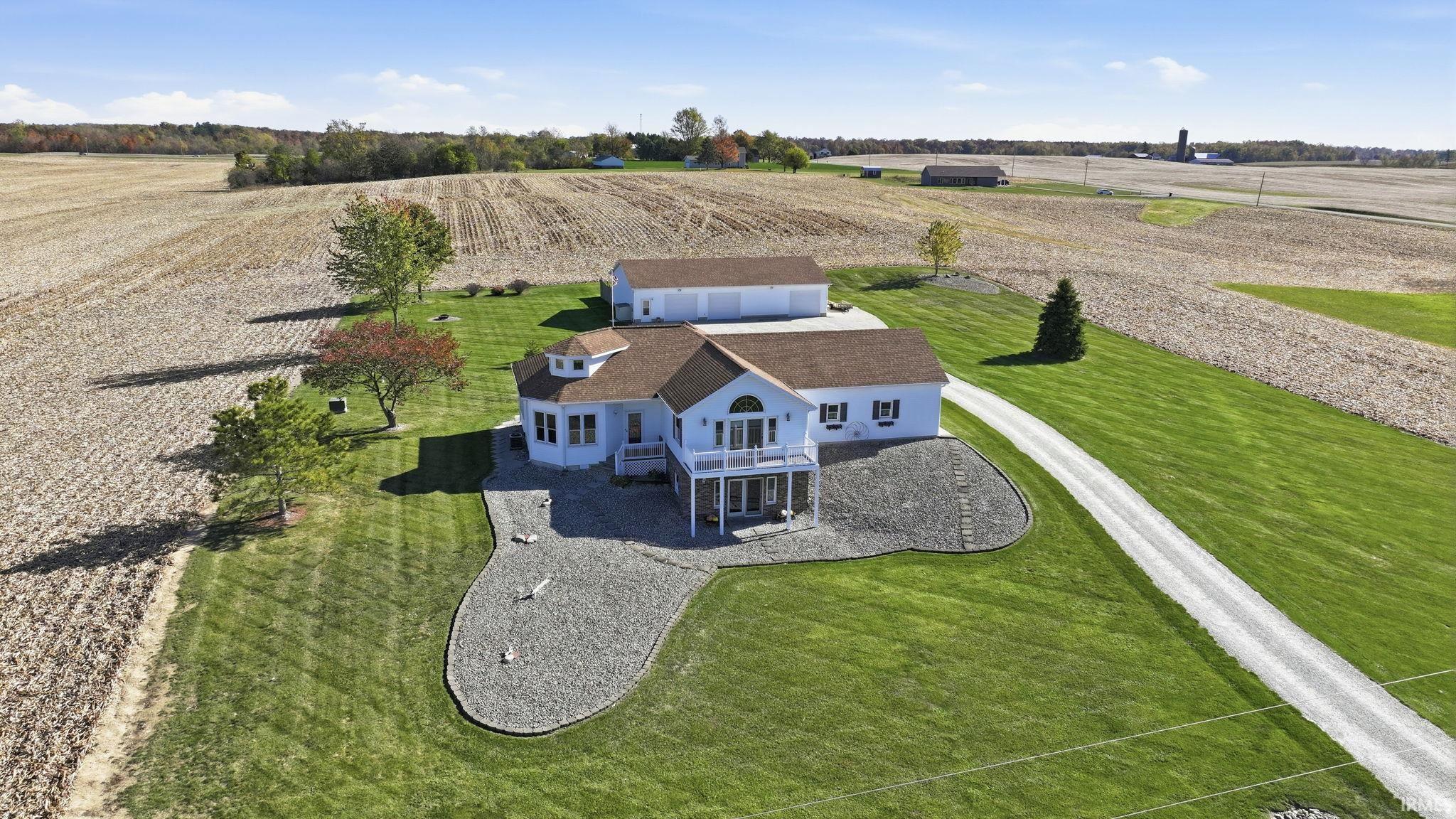 Single-story residence featuring a shingled roof, elevated deck, detached three-car garage, gravel landscaping, and a long driveway situated on expansive acreage