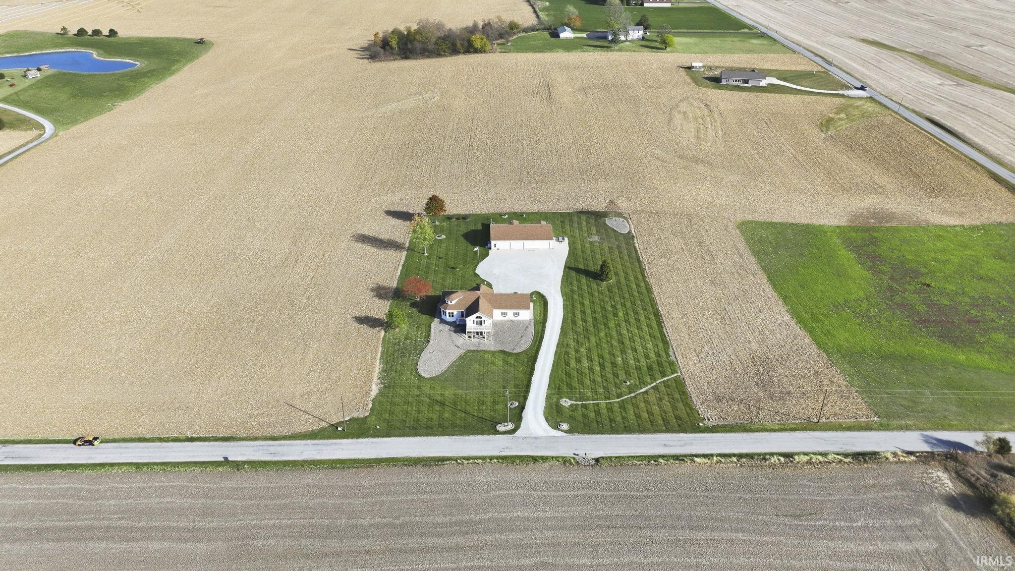 Aerial view featuring a single-story residence, a detached garage, an expansive lawn, and a paved concrete driveway