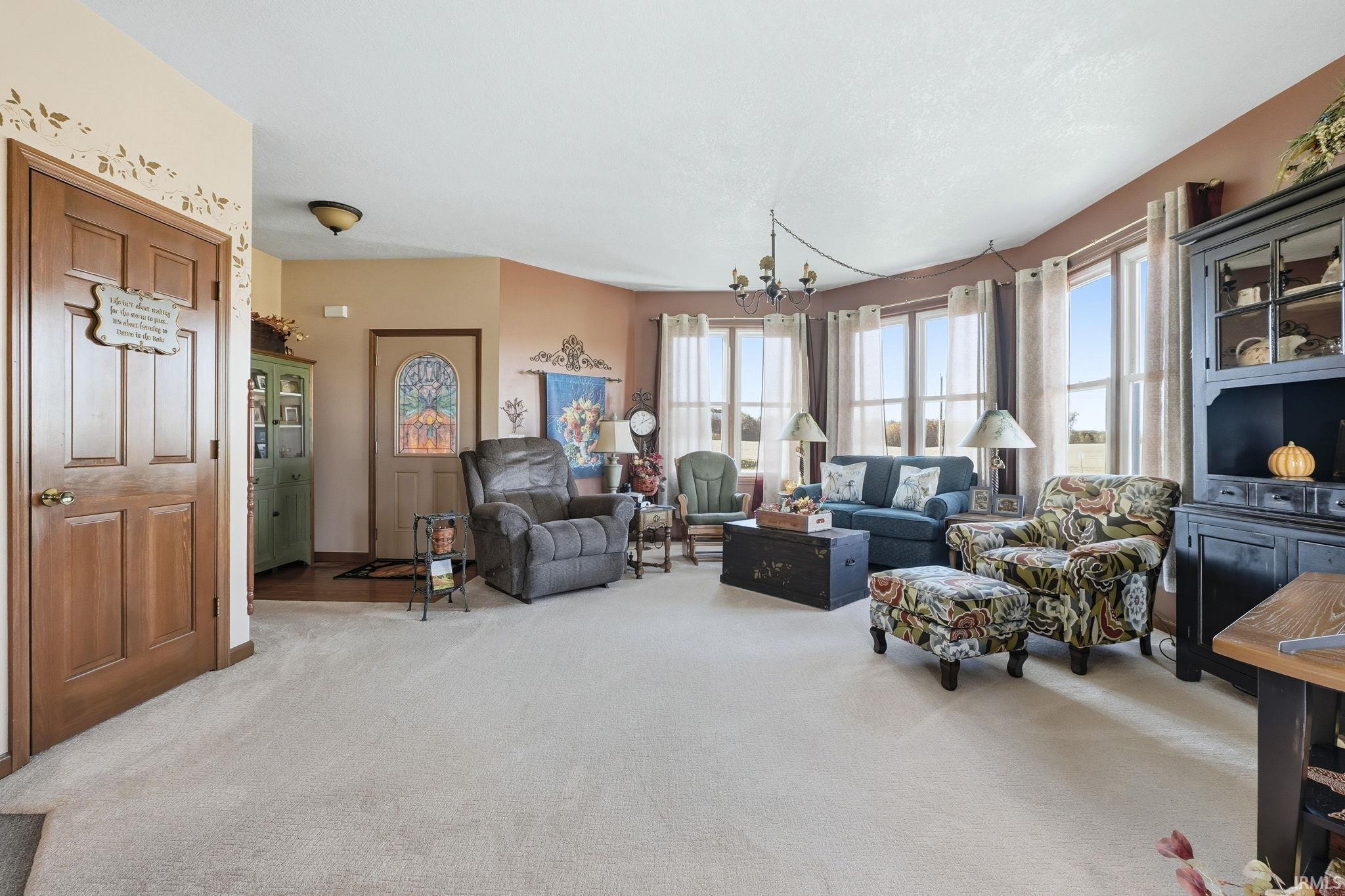 Living area featuring a bay window, six-panel wood door, exterior door with stained glass insert, and a multi-arm chandelier
