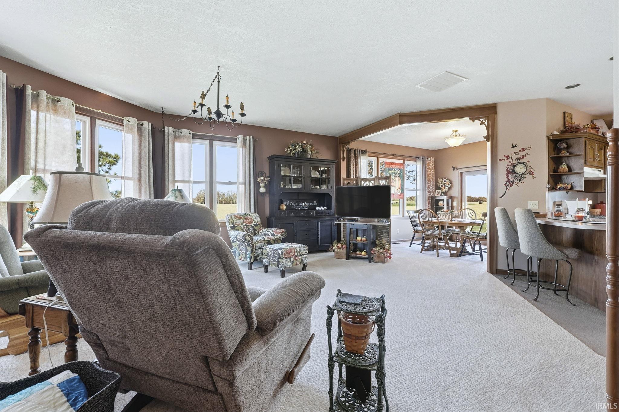 Open-concept interior featuring oversized windows, decorative wooden archway, wall-to-wall carpeting, and a built-in kitchen breakfast bar