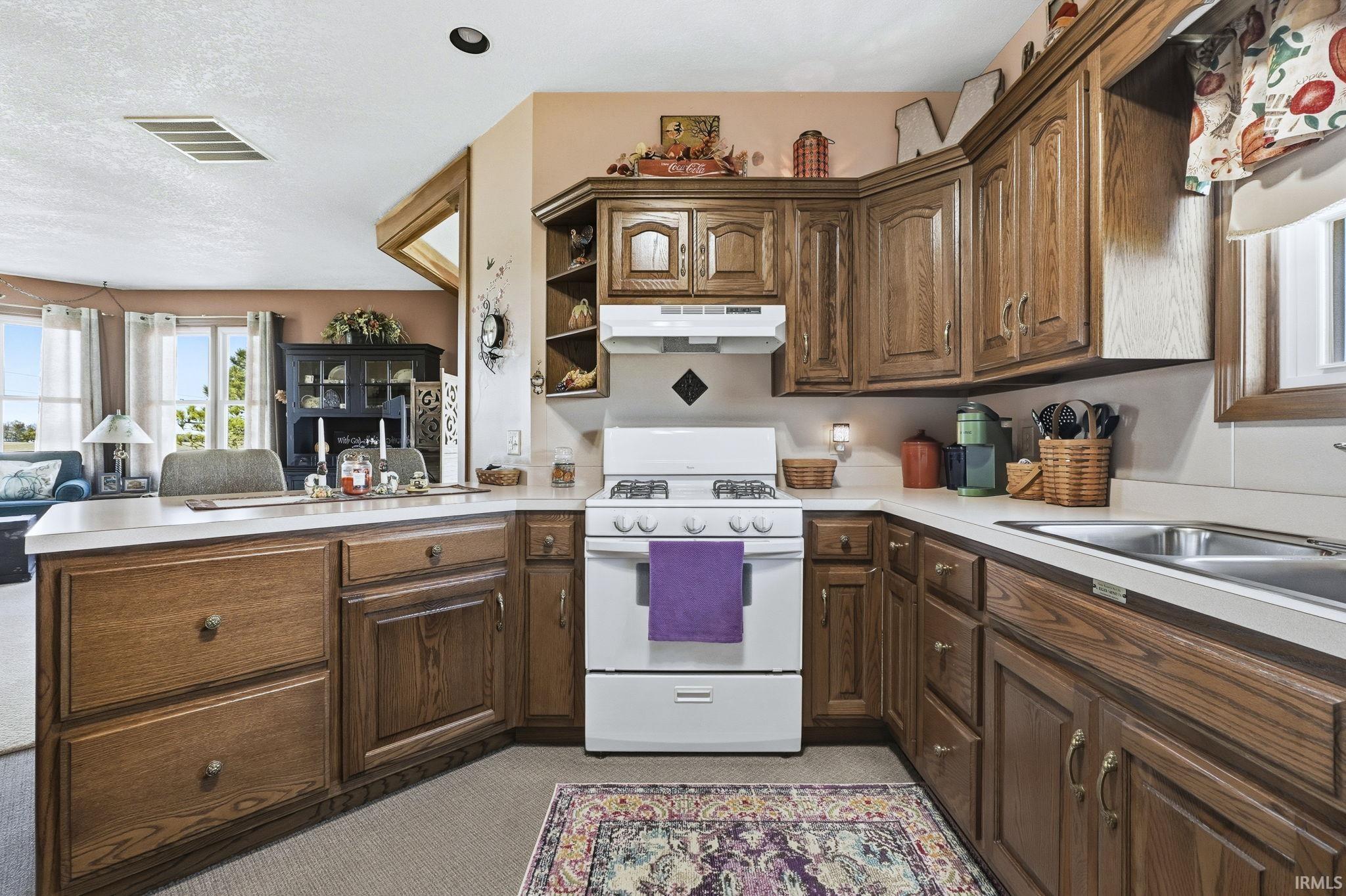 Kitchen featuring oak cabinetry, solid-surface countertops, dual-basin stainless steel sink, and a white gas range with a matching range hood