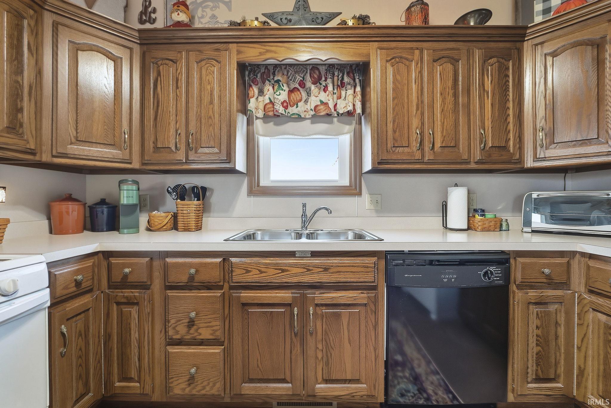 Kitchen featuring wood cabinetry, solid-surface countertops, double-basin stainless steel sink with arched faucet, and built-in dishwasher