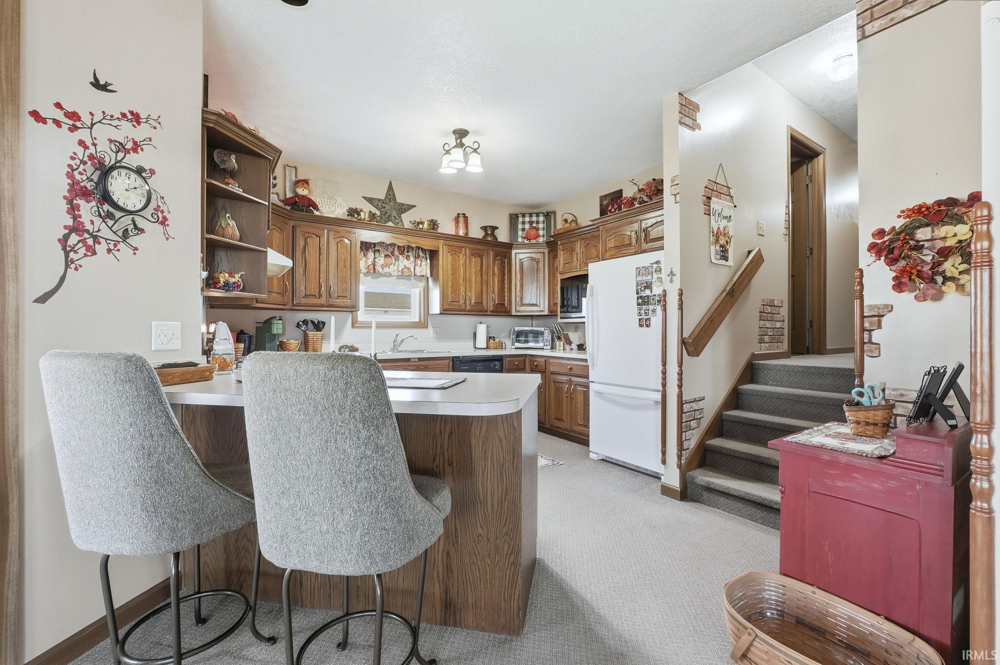 Kitchen featuring wood cabinetry, a breakfast bar with laminate countertop, built-in microwave, and stairwell with a wooden handrail