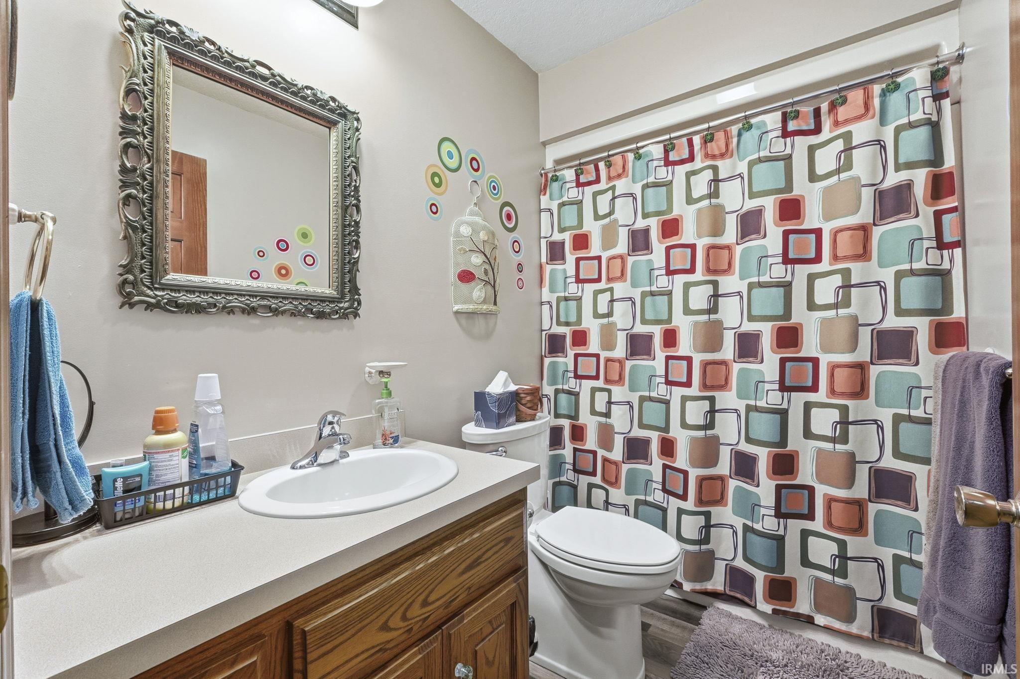 Bathroom featuring a wood-finish vanity with a molded countertop and integrated sink, a chrome faucet, and an ornate wall-mounted mirror
