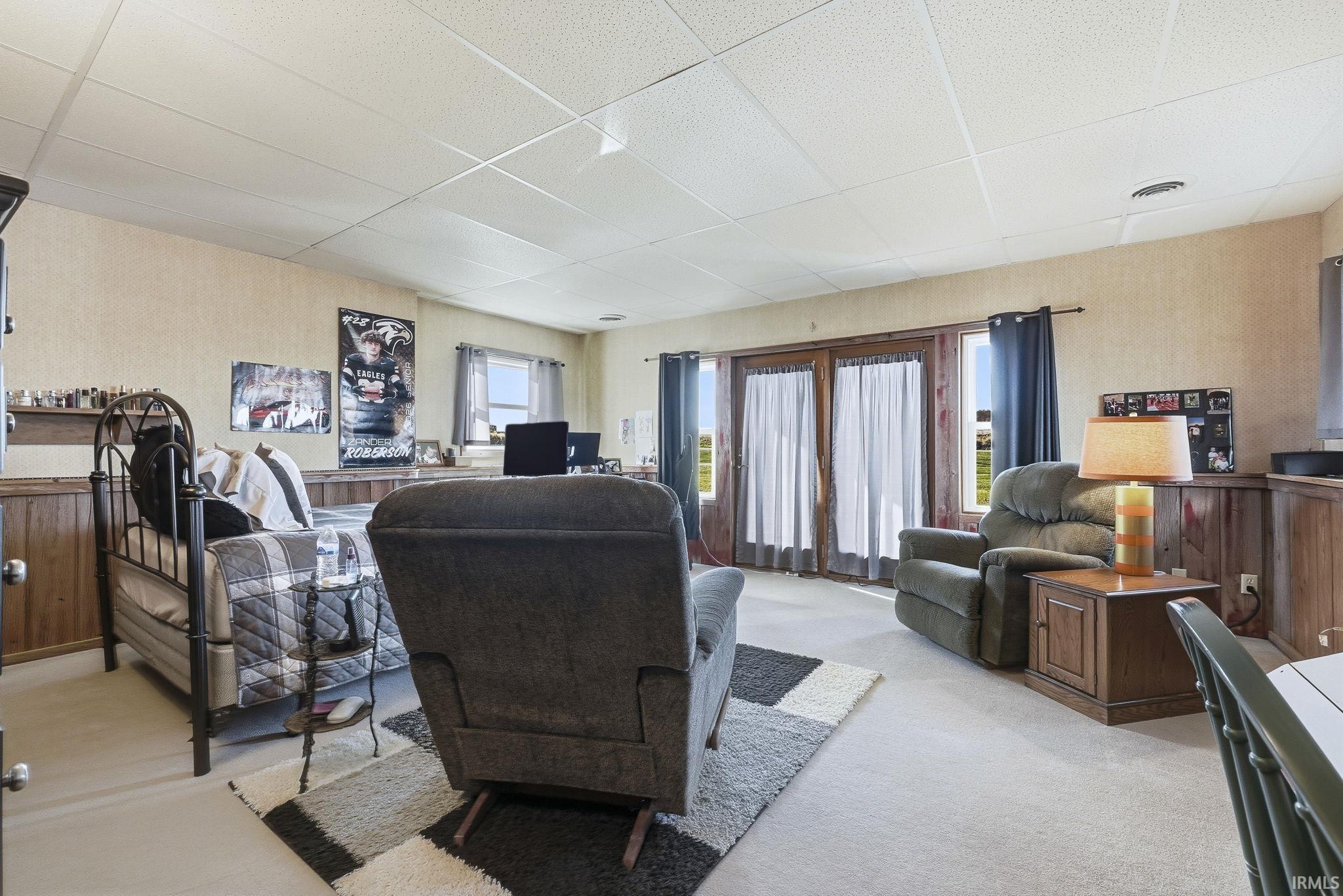 Interior space featuring wood-paneled wainscoting, a drop ceiling, carpeted flooring, and glass-paneled double doors
