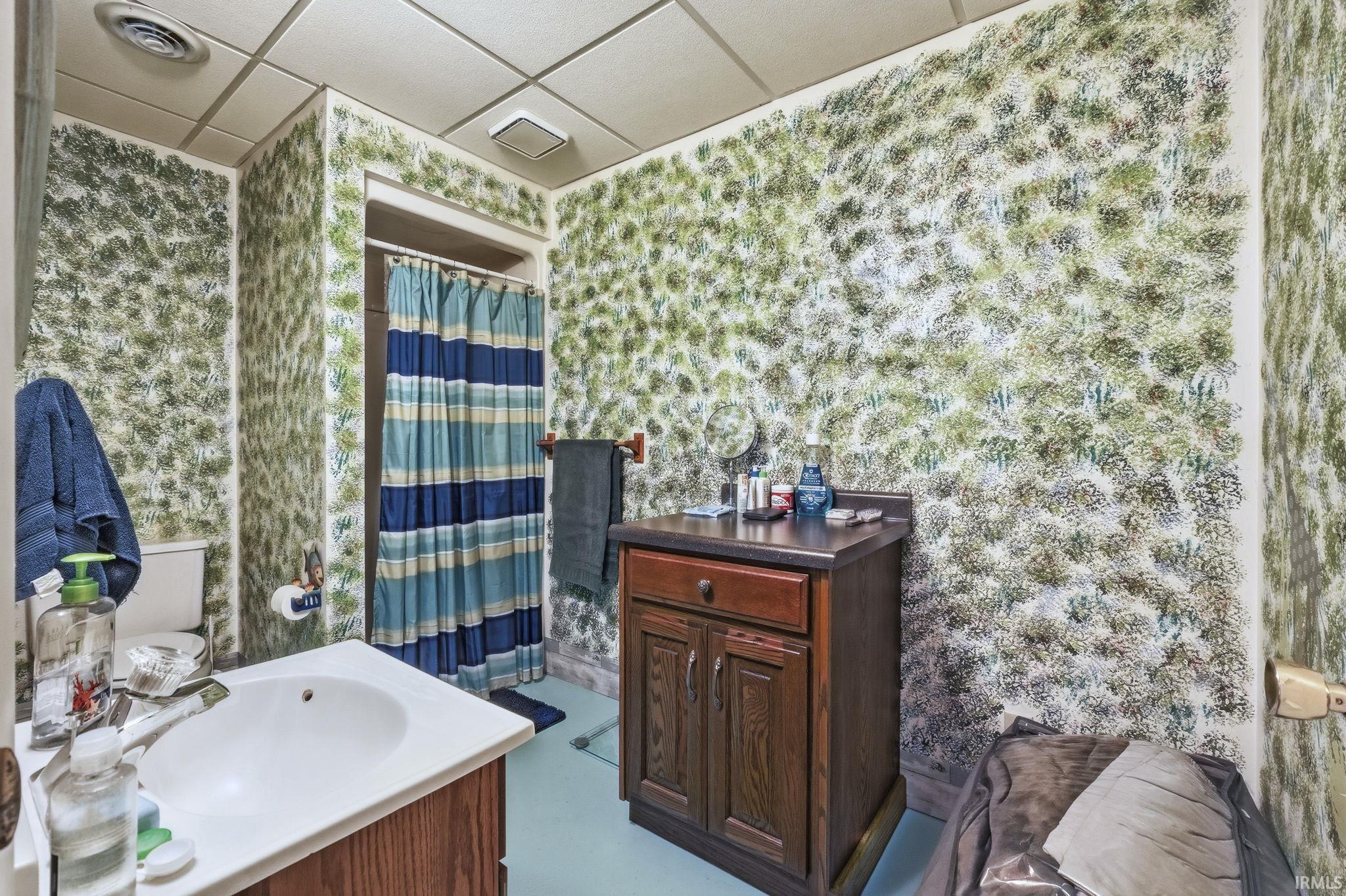 Bathroom featuring wood-finish cabinetry, a white countertop with an integrated basin, and a drop-in ceiling system
