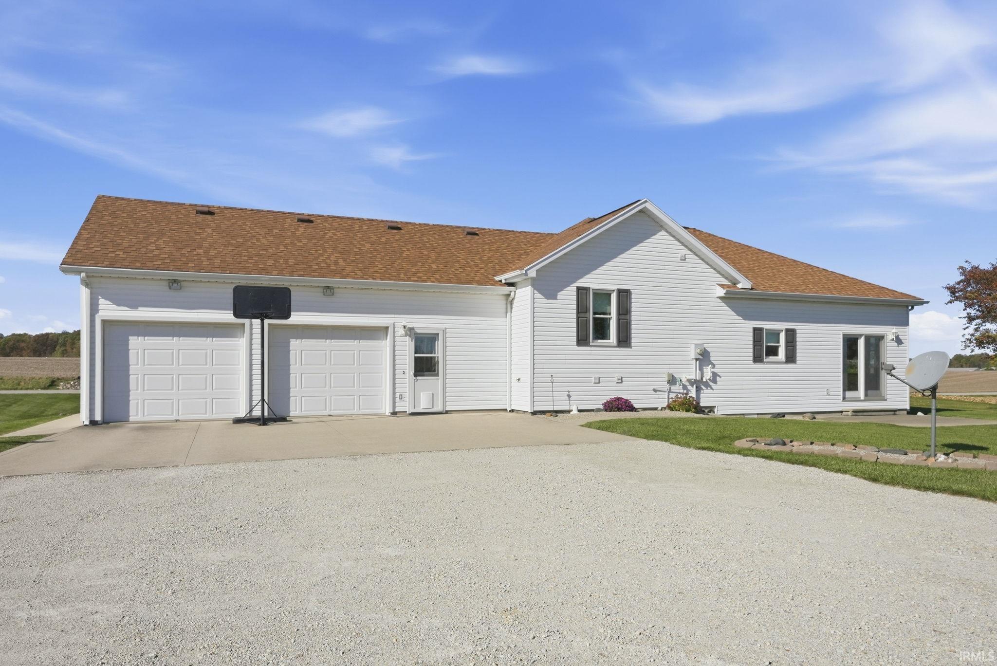Exterior profile featuring white vinyl siding, a multi-gabled roofline, a two-car garage, and an expansive gravel driveway