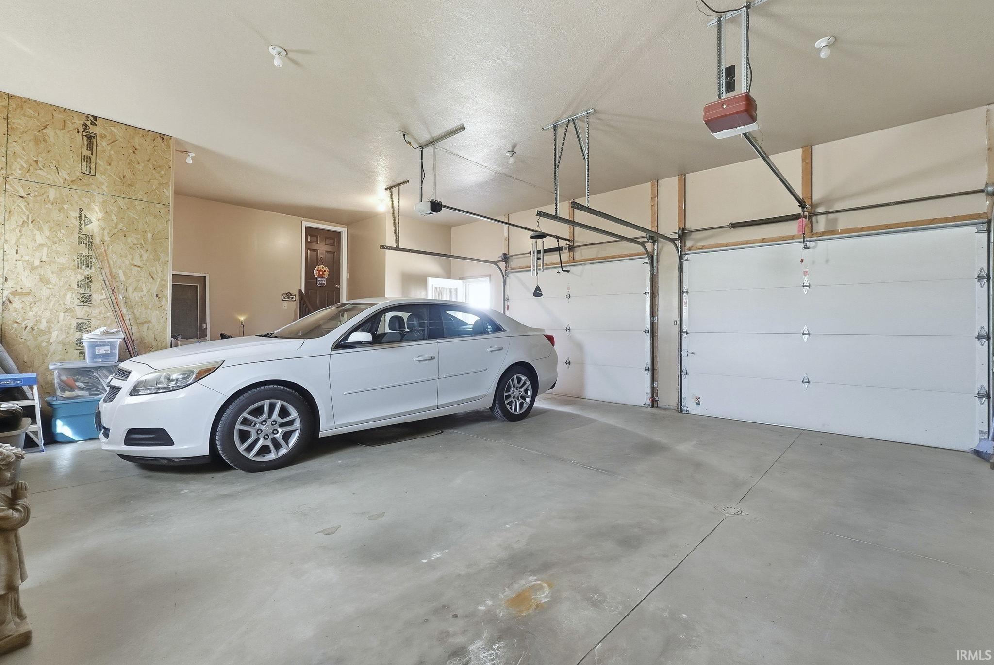 Attached three-car garage featuring dual overhead motorized door openers, concrete flooring, and exposed interior wall paneling