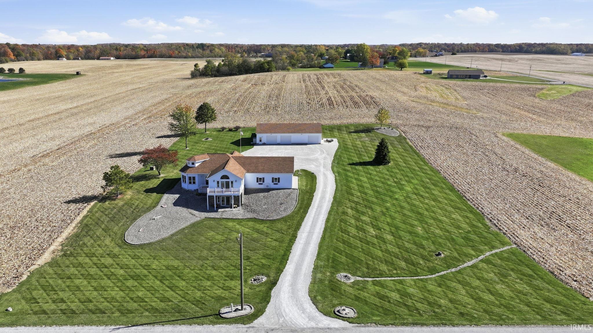 Expansive rural property featuring a multi-level residence, detached garage, gravel driveway, manicured lawn, and mature landscaping