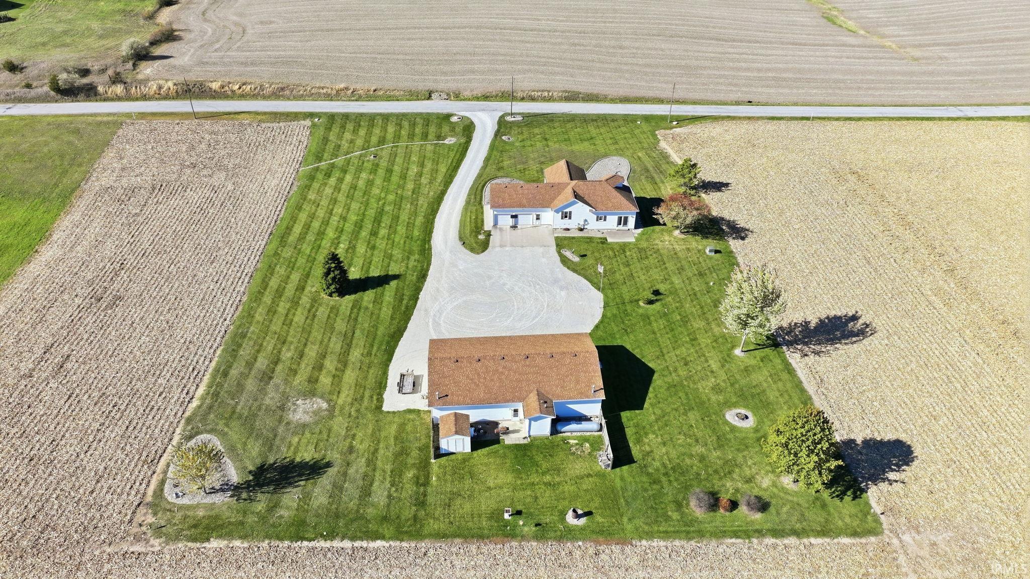 Aerial perspective of a detached residence and secondary structure, featuring expansive acreage, a sprawling manicured lawn, and a long gravel driveway