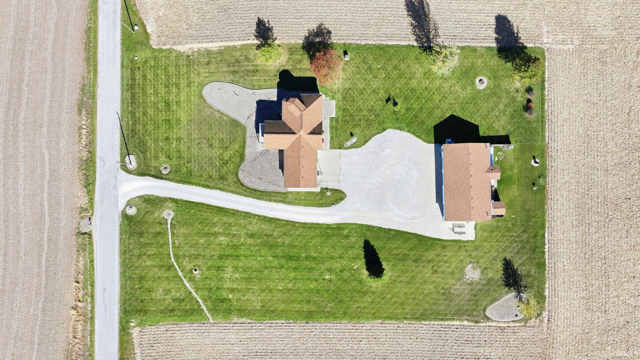 Aerial view of the parcel featuring a primary residence and a detached structure, expansive manicured grounds, an extensive gravel driveway, and mature perimeter trees