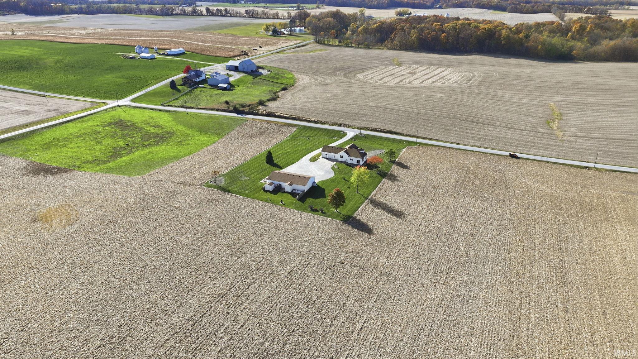 Aerial view featuring a multi-structure property, expansive acreage, paved driveway, and established landscape