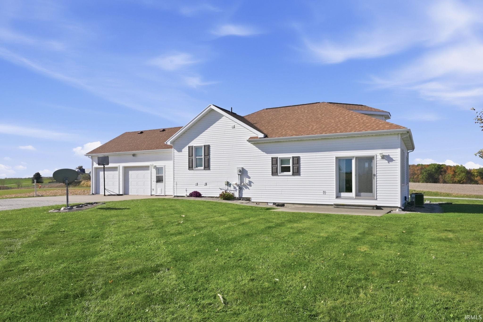 White vinyl siding exterior featuring a multi-car garage, shingled roof, sliding glass door, and a concrete patio