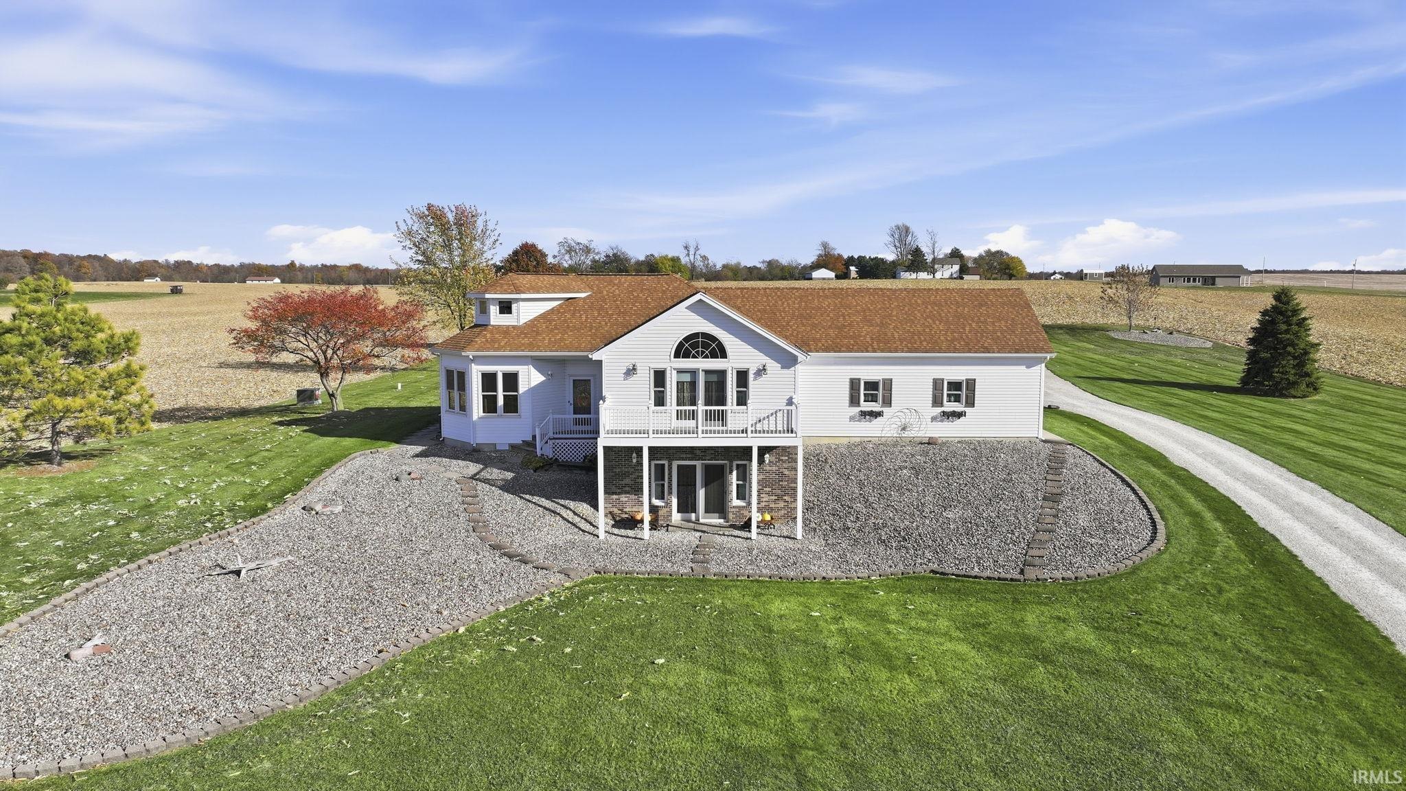 Exterior featuring white siding, a stone veneer foundation, elevated wooden deck, shingled roof, and a gravel driveway