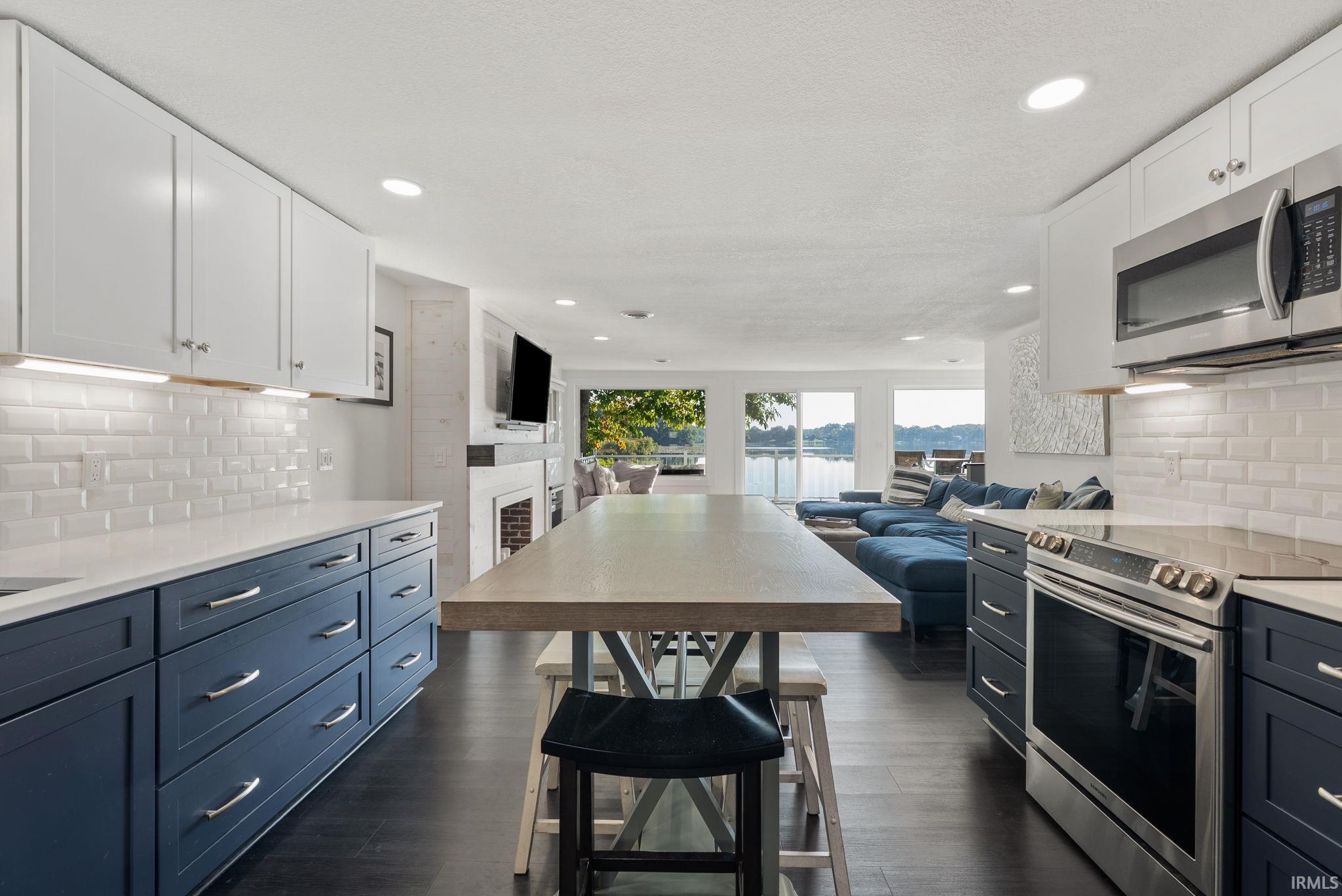 Kitchen featuring two-tone cabinetry, stainless steel appliances, a subway tile backsplash, and dark wood-finish flooring