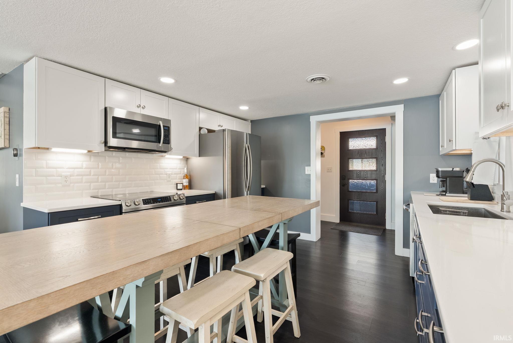 Gourmet kitchen featuring stainless steel appliances, white subway tile backsplash, white countertops, and dark wood-finish flooring