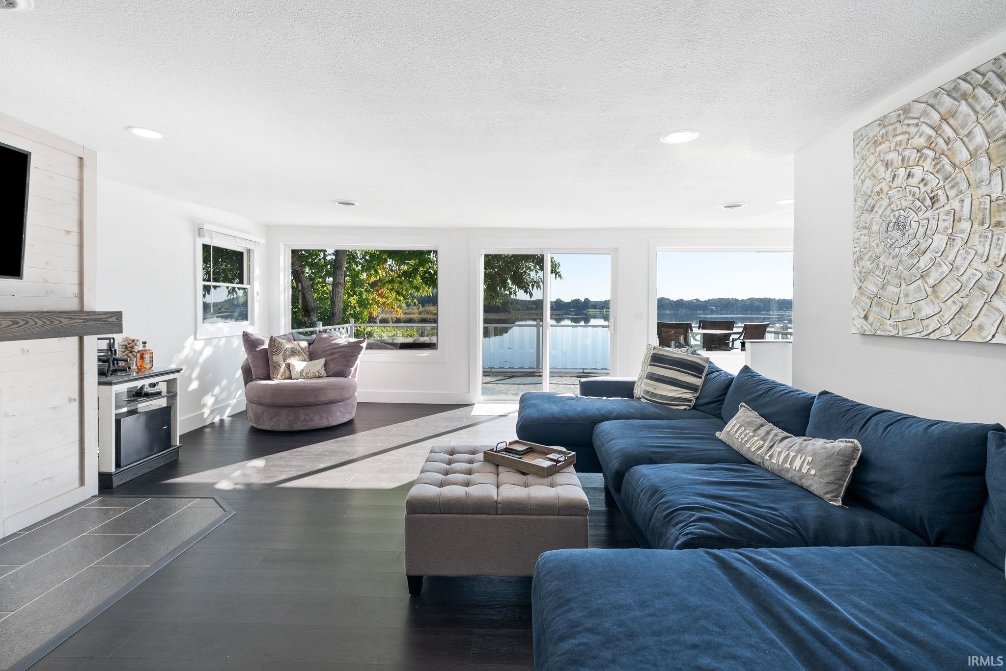 Open-concept living space featuring a blue upholstered sectional, dark polished concrete flooring, and extensive sliding glass doors opening to waterfront scenery