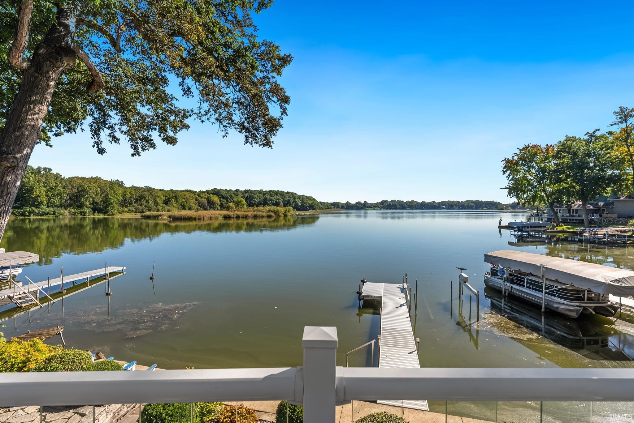 Expansive lakefront setting featuring multiple docks, a boat lift, and mature trees