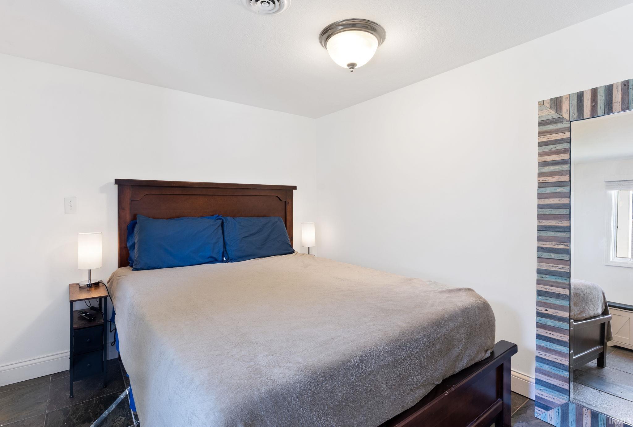Recessed ceiling light, dark wood headboard, dark wood bed frame, dark tile flooring, ceiling-mounted light fixture