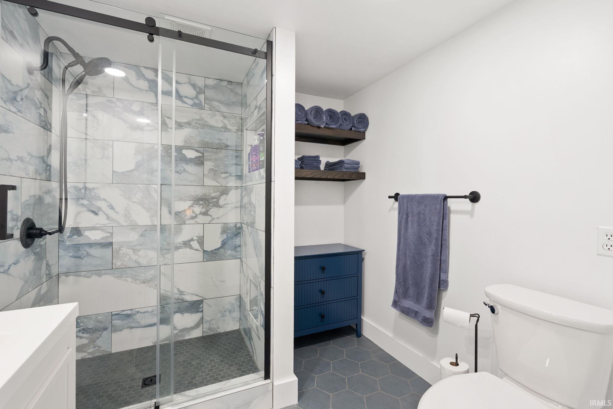 Shower with glass enclosure, black hardware, and blue-toned tile, complemented by hexagonal floor tiling