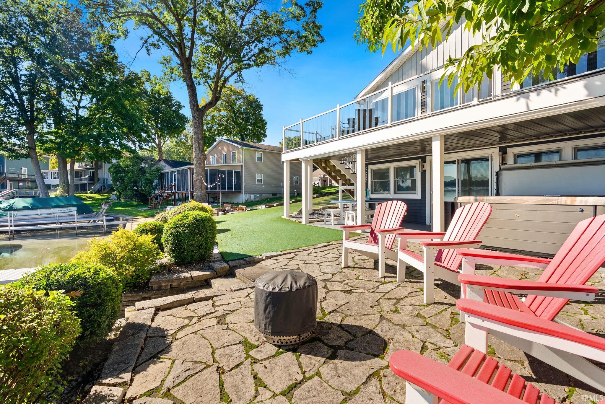 Stone patio with a fire pit, artificial turf, and mature trees
